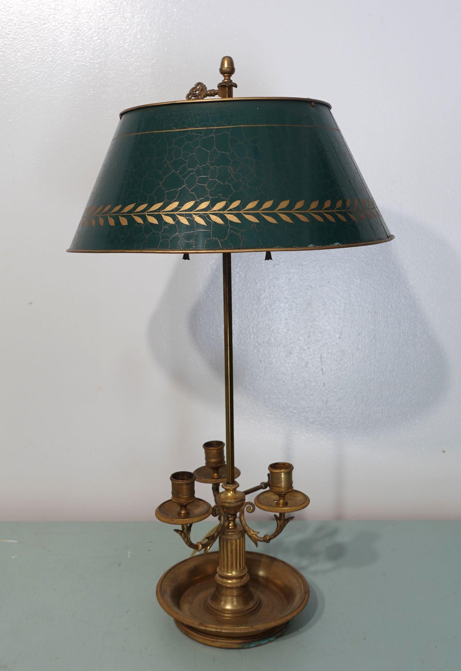 A 19th-century bouillotte lamp in the Louis XVI taste, the steel shaft with brass laurel ring and arrowhead screw, supporting a green tole shade, all above a base of three brass candle arms with stylized supports, set upon a fluted column and engine