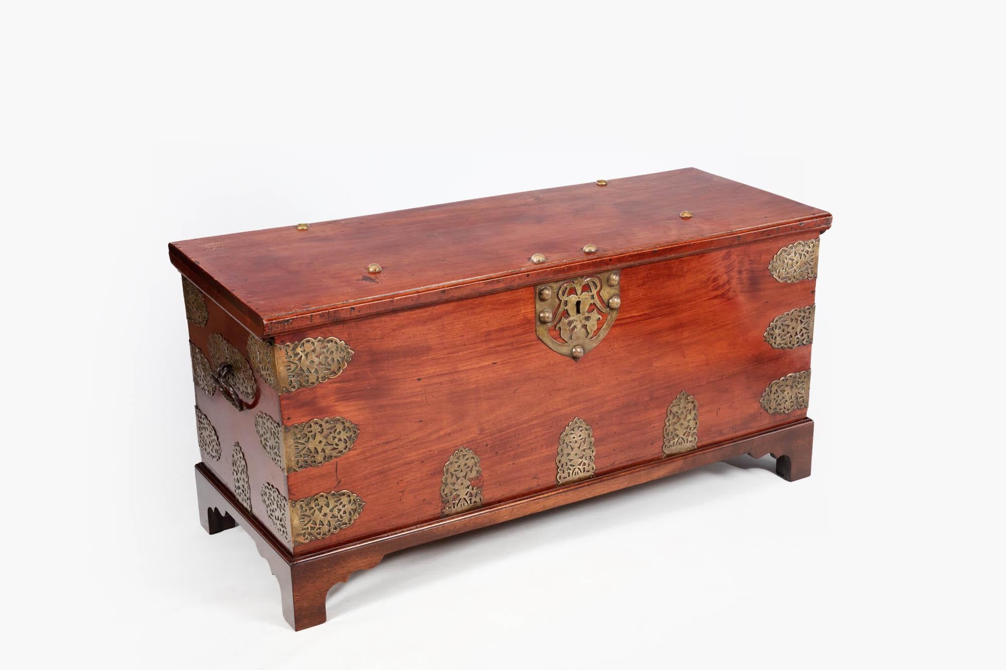 19th Century brass bound hardwood chest decorated with shaped pierced mounts, with hinged molded rectangular top, the front with a pierced lock-plate, nail head decoration and the sides with carrying handles. The piece sits on ogee bracket feet. The