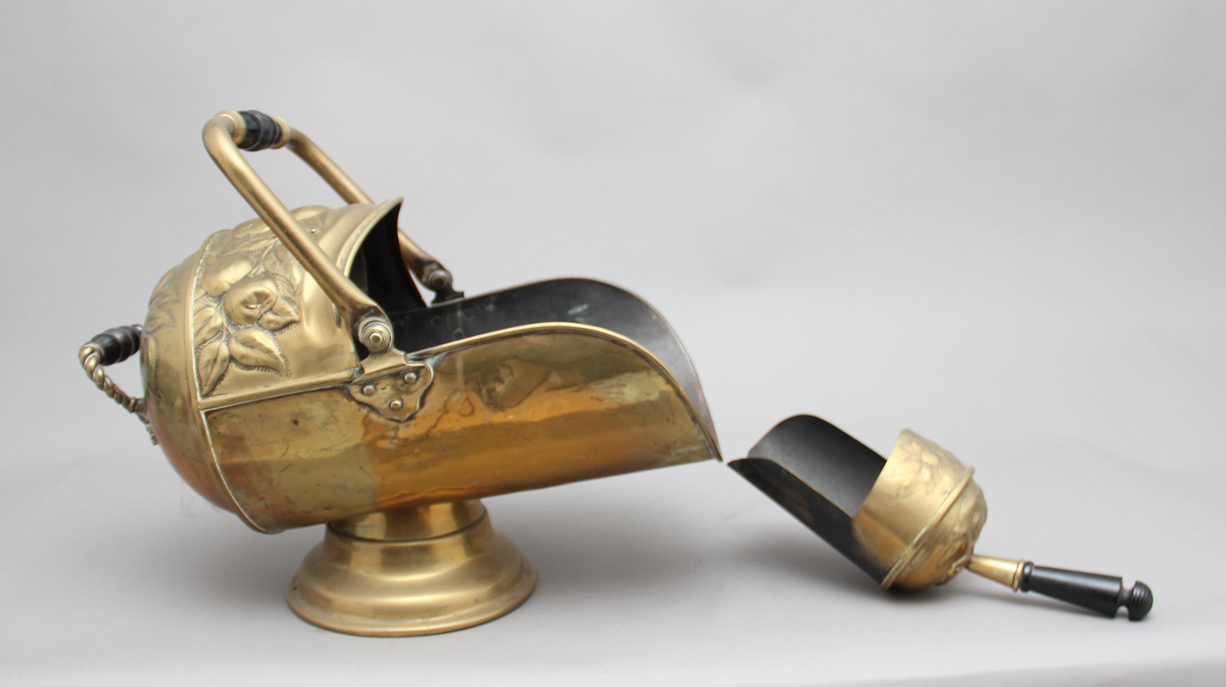 19th century brass coal scuttle with coal shovel, the helmet shaped coal scuttle having carved floral decoration, shaped brass handle with turned wooden middle section, supported on a circular brass plinth, circa 1860.
 