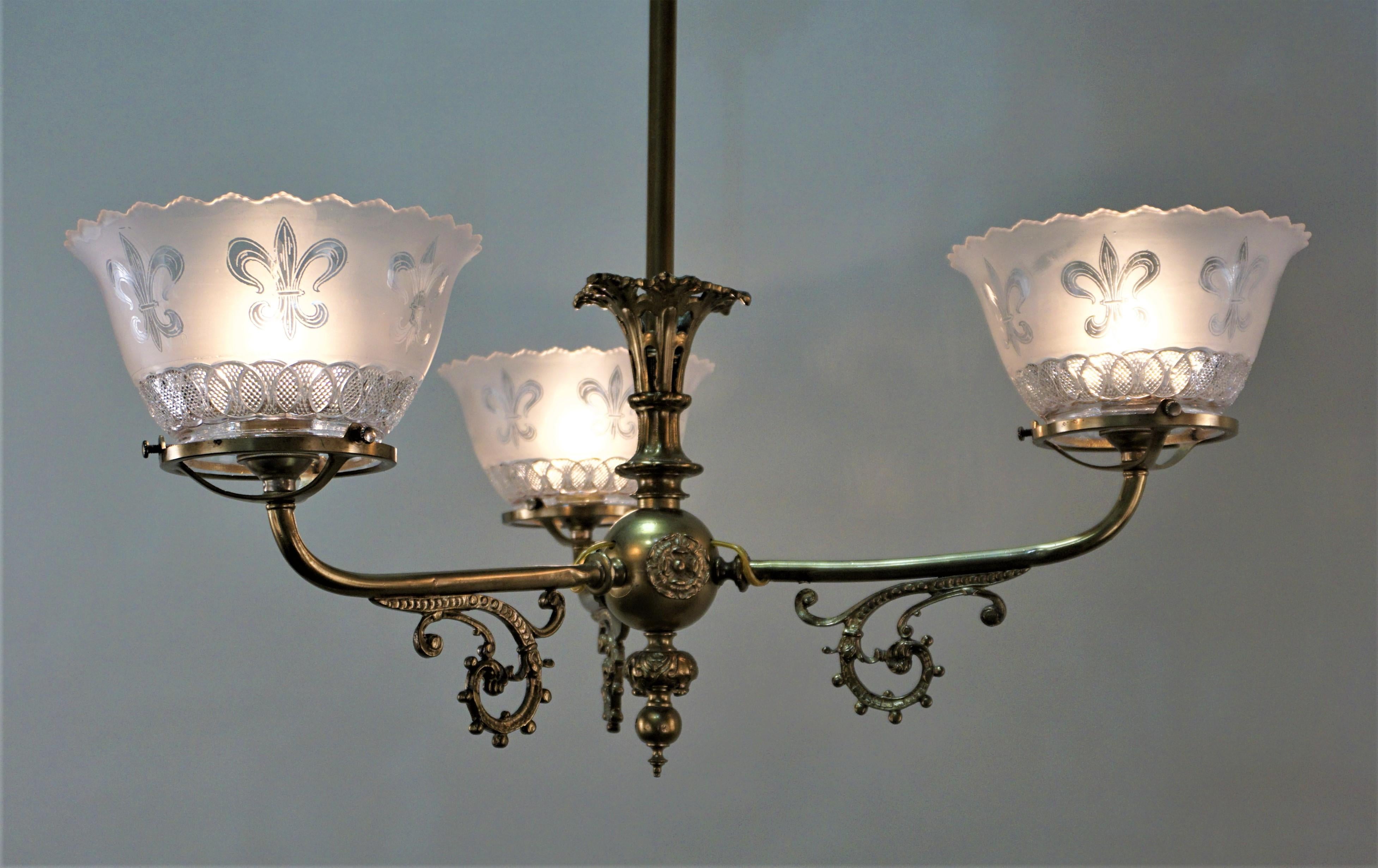 19th century electrified three-arm brass gas chandelier with glass shades.