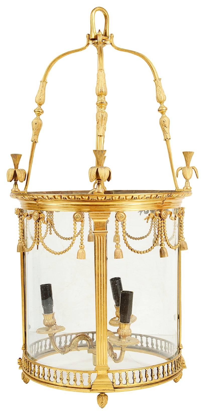 A good quality French, late 19th century brass hall lantern, having swag and tassel decoration, fluted columns and a gallery to the base. Bowed glass panels and a three branch sconce to the centre.