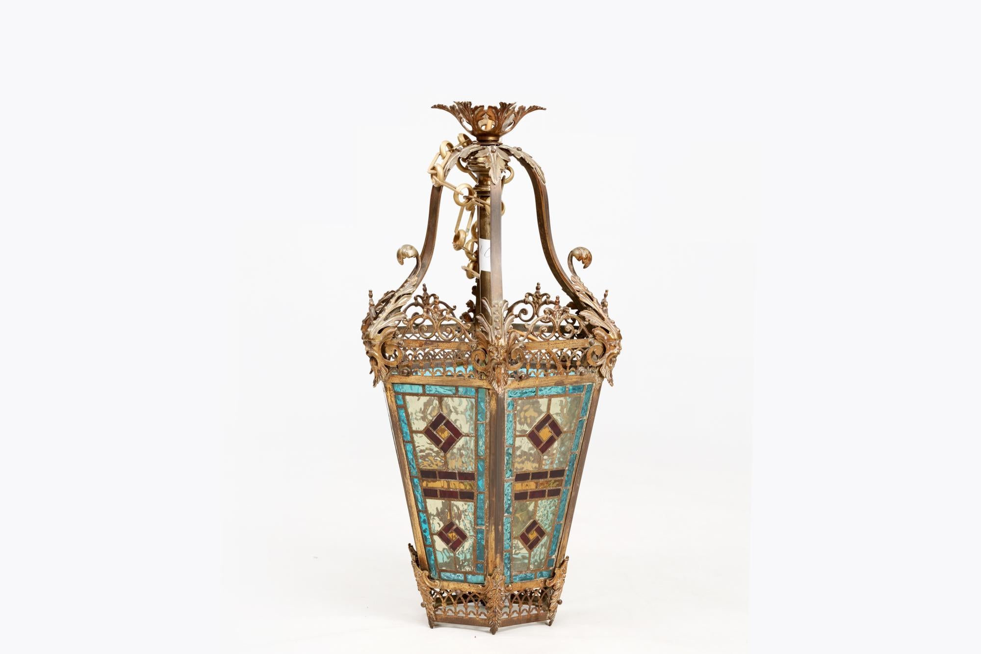 19th Century brass hall lantern with original stained glass panels. The frame with pierced brass gothic-style arches is complimented by bearded figureheads to the corners terminating in scrolled foliate detail.