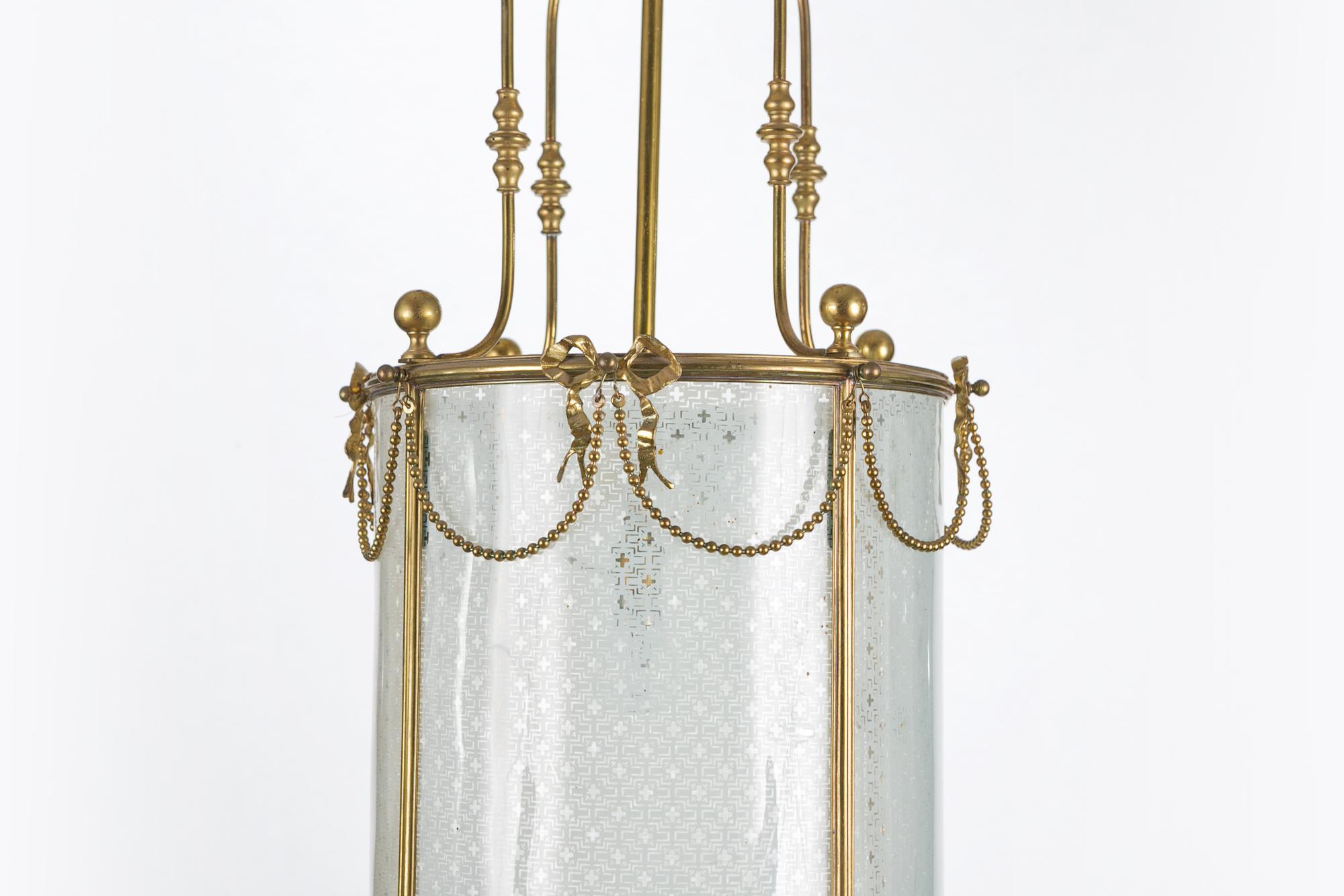 19th century brass lantern of cylindrical form with decorative frieze of beaded swags, supported by ribbon bows and four glass panels.
