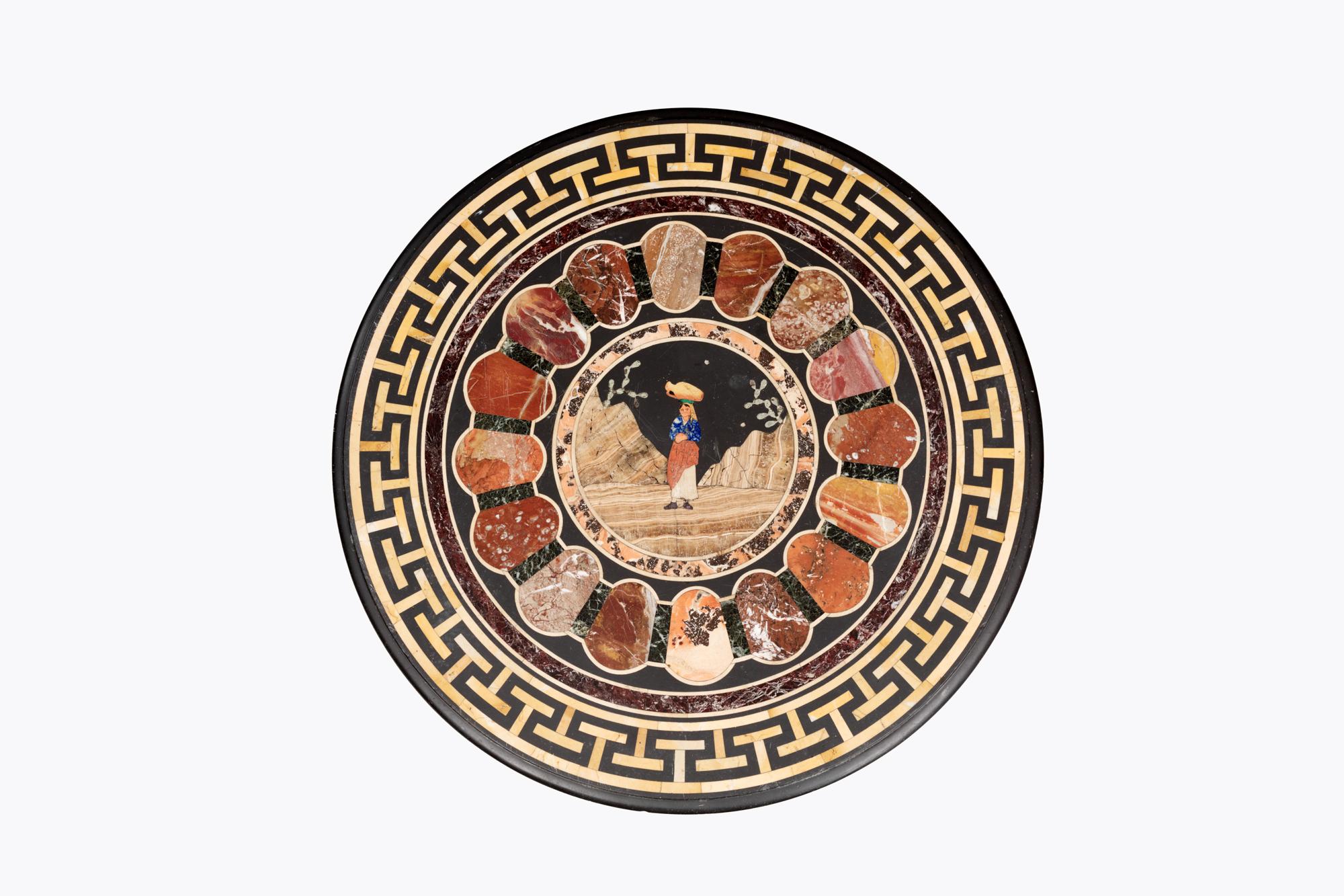 Messingmontierter runder Couchtisch mit Speimanplatte aus dem 19. Jahrhundert. Die zentrale Tafel aus Edelstein stellt eine Szene mit einem Wasserträger in einer Berglandschaft dar. Dieser ist von einem Ring aus kostbaren Marmormustern umgeben und