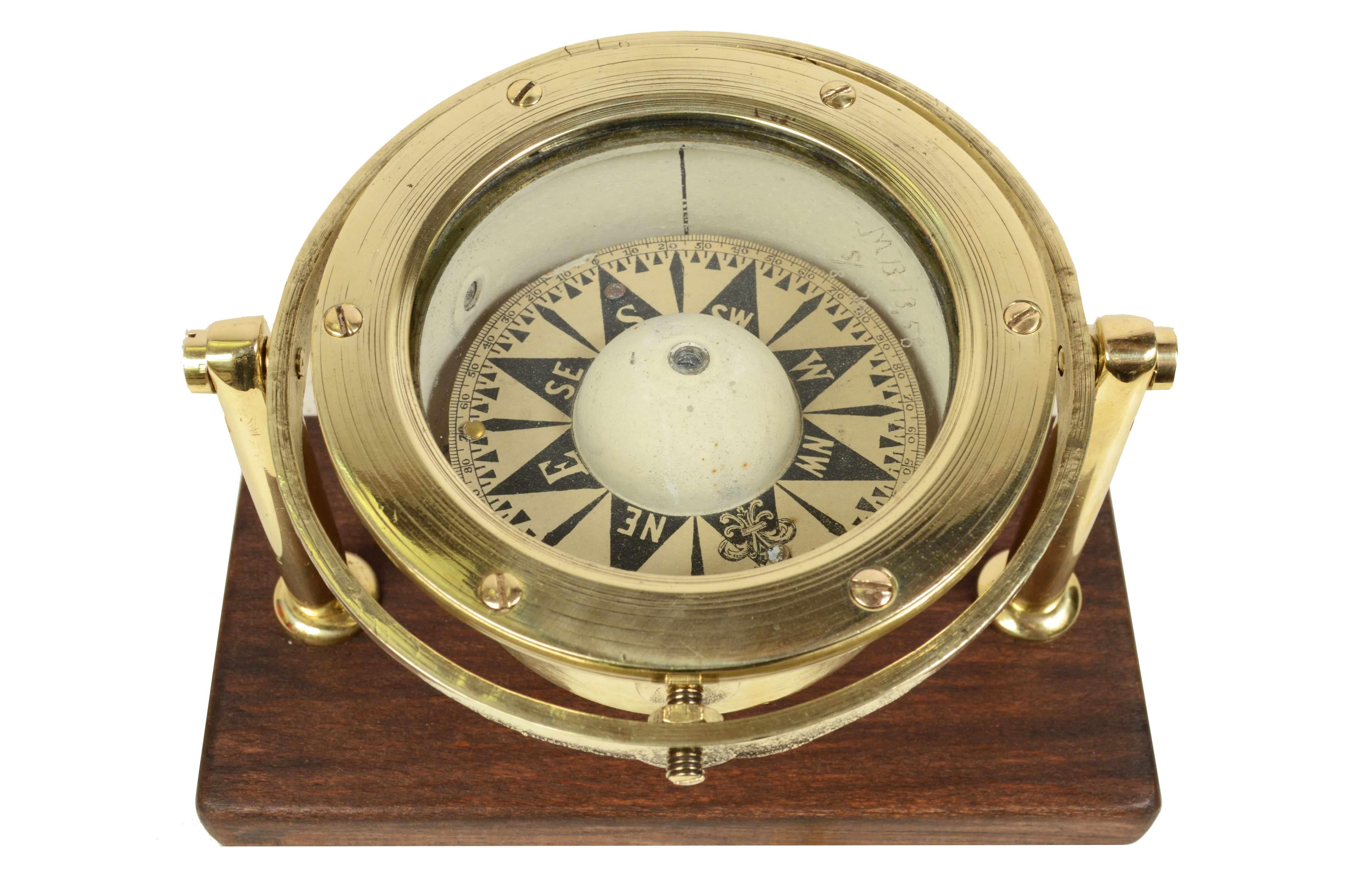 Brass and glass compass on universal joint from the end of the 19th century. Mounted on custom wood board. The compass consists of a cylindrical brass container, called a mortar, with double glass on the bottom of which is fixed a hard metal stem,