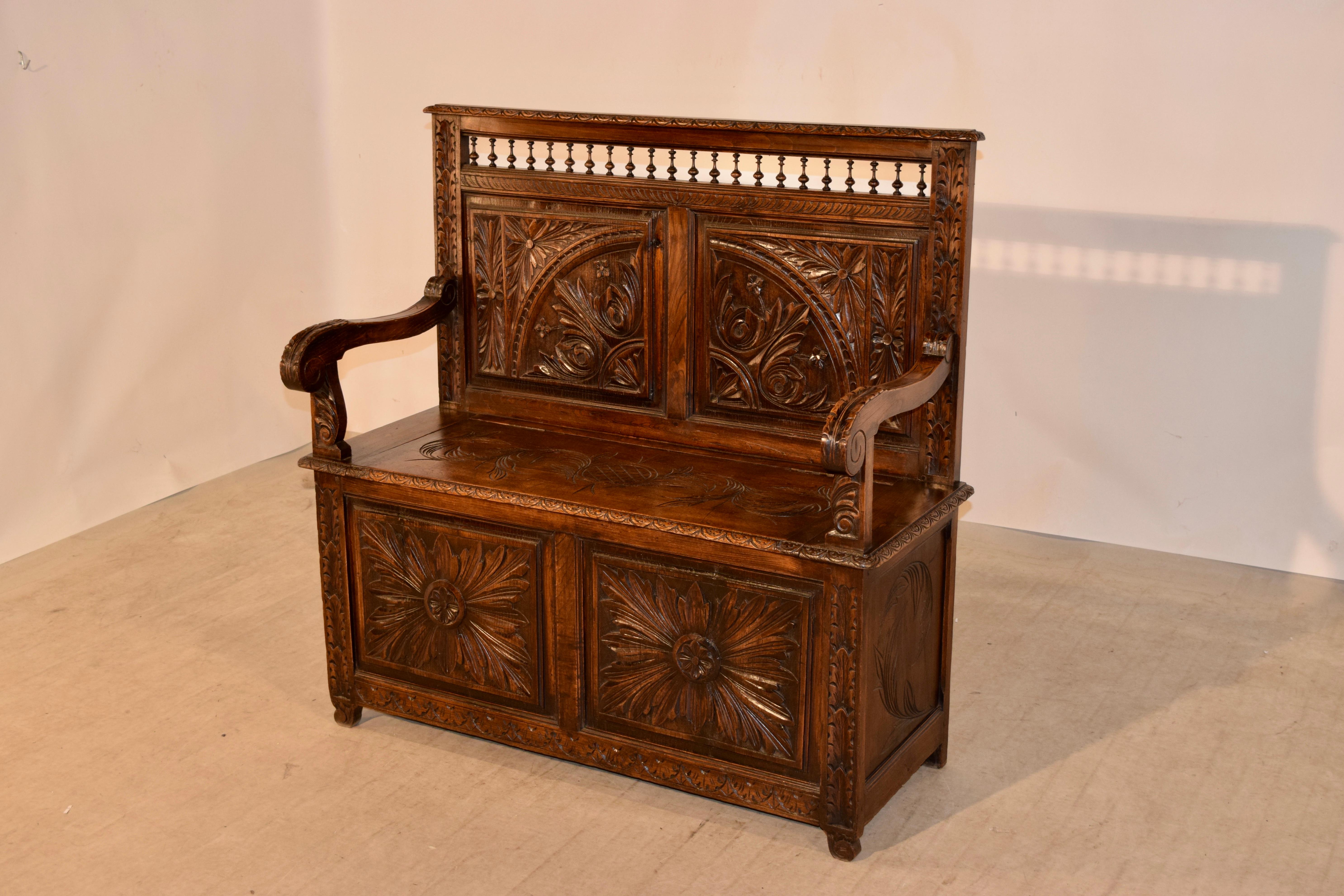 19th century oak bench from Brittany in France. The top is a hand carved decorated molded edge following down to the typical hand-turned spindle design over two hand carved raised panels over a seat which lifts to reveal storage and has two hand