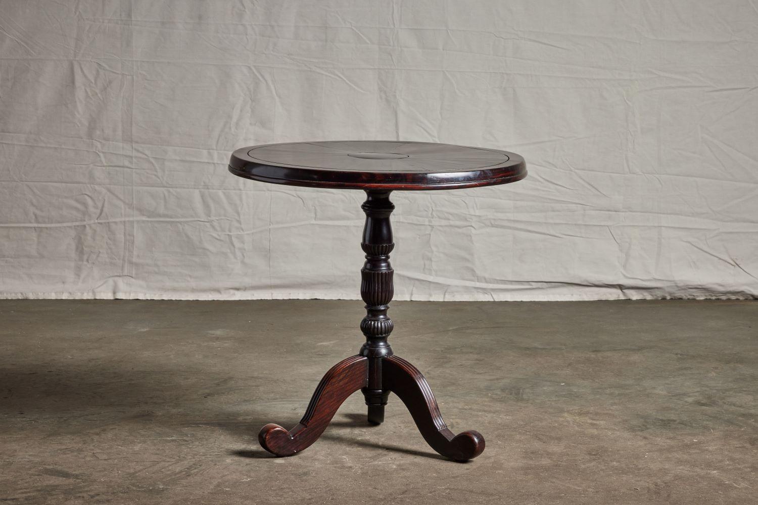 A 19th century British Colonial ebony pedestal table featuring a turned and fluted pedestal and three carved legs.