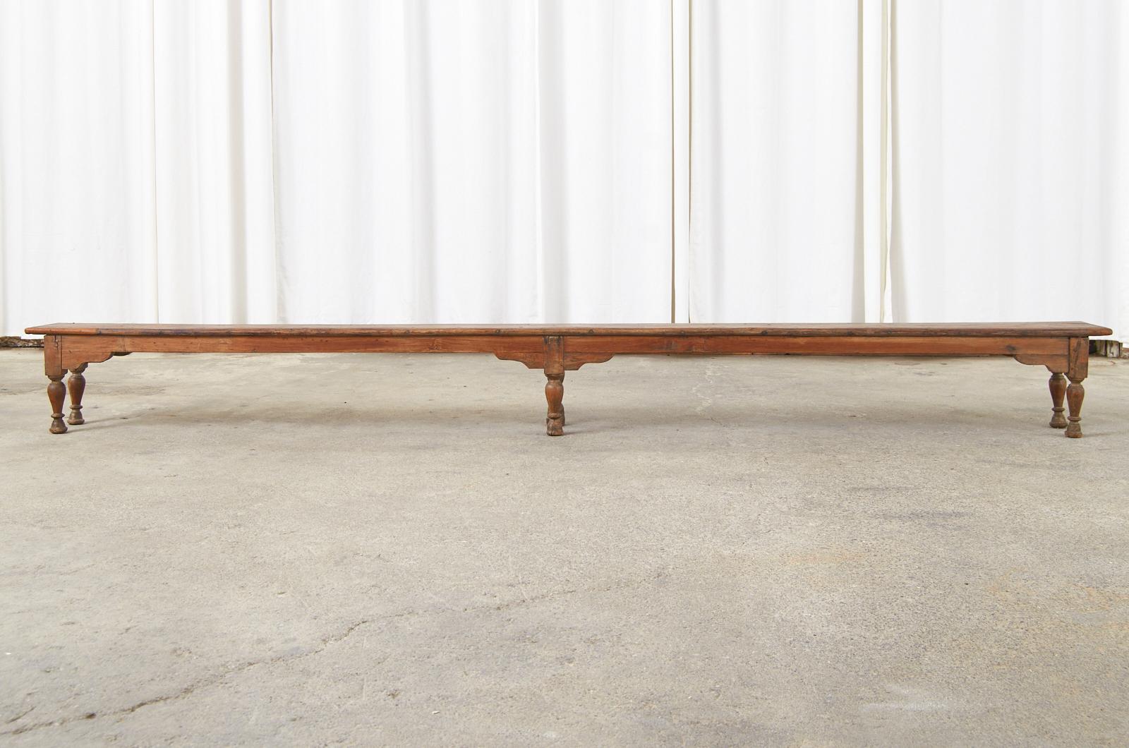 Monumental 19th century low display table, console table, or bench measuring over 10 feet long. British Colonial handcrafted from hardwood including teak. The long plank top has breadboard ends and is supported by turned legs ending with bell shaped