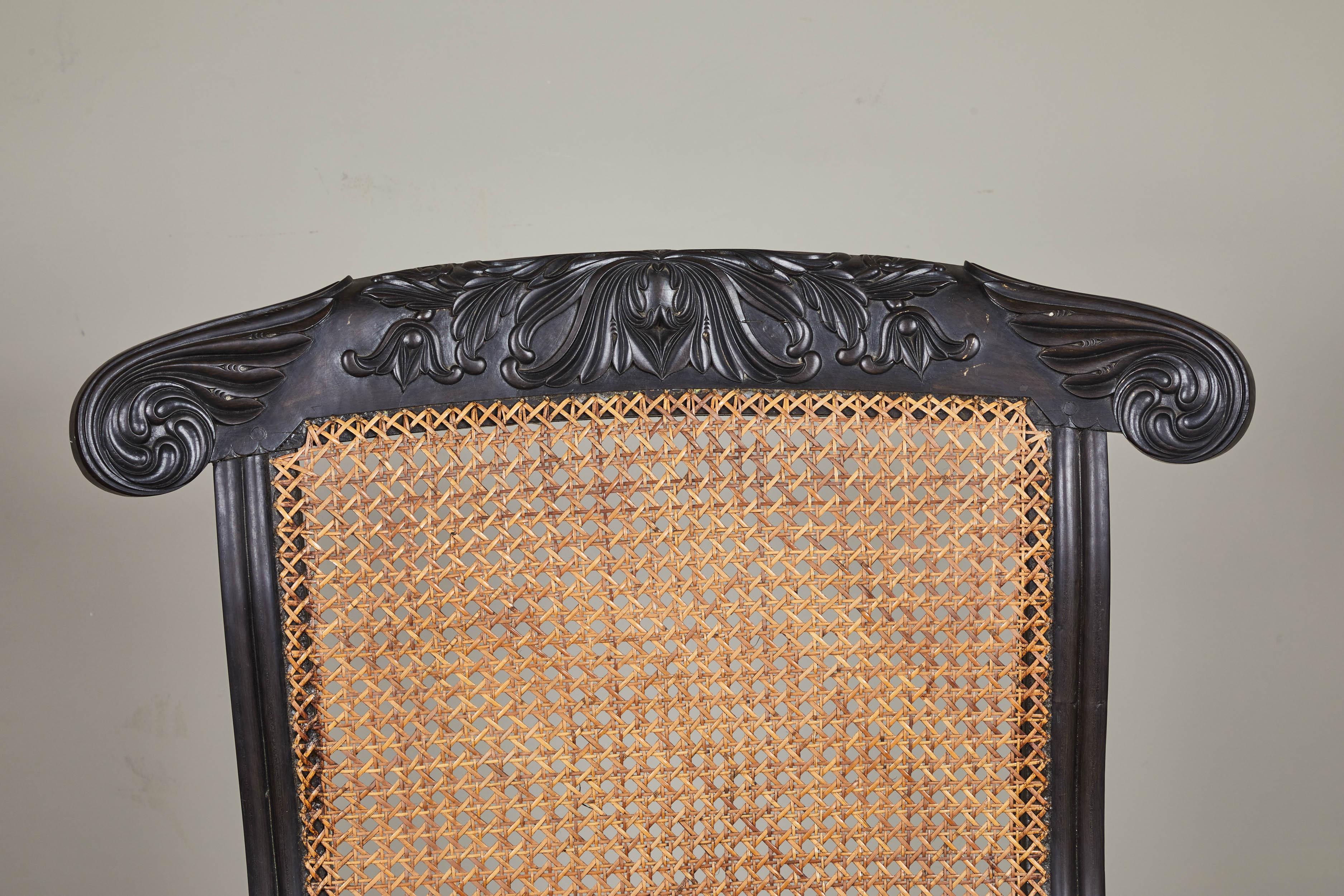 A 19th century British Colonial Ebony chair with carved back and feet. Caned seat with scrolled arms.