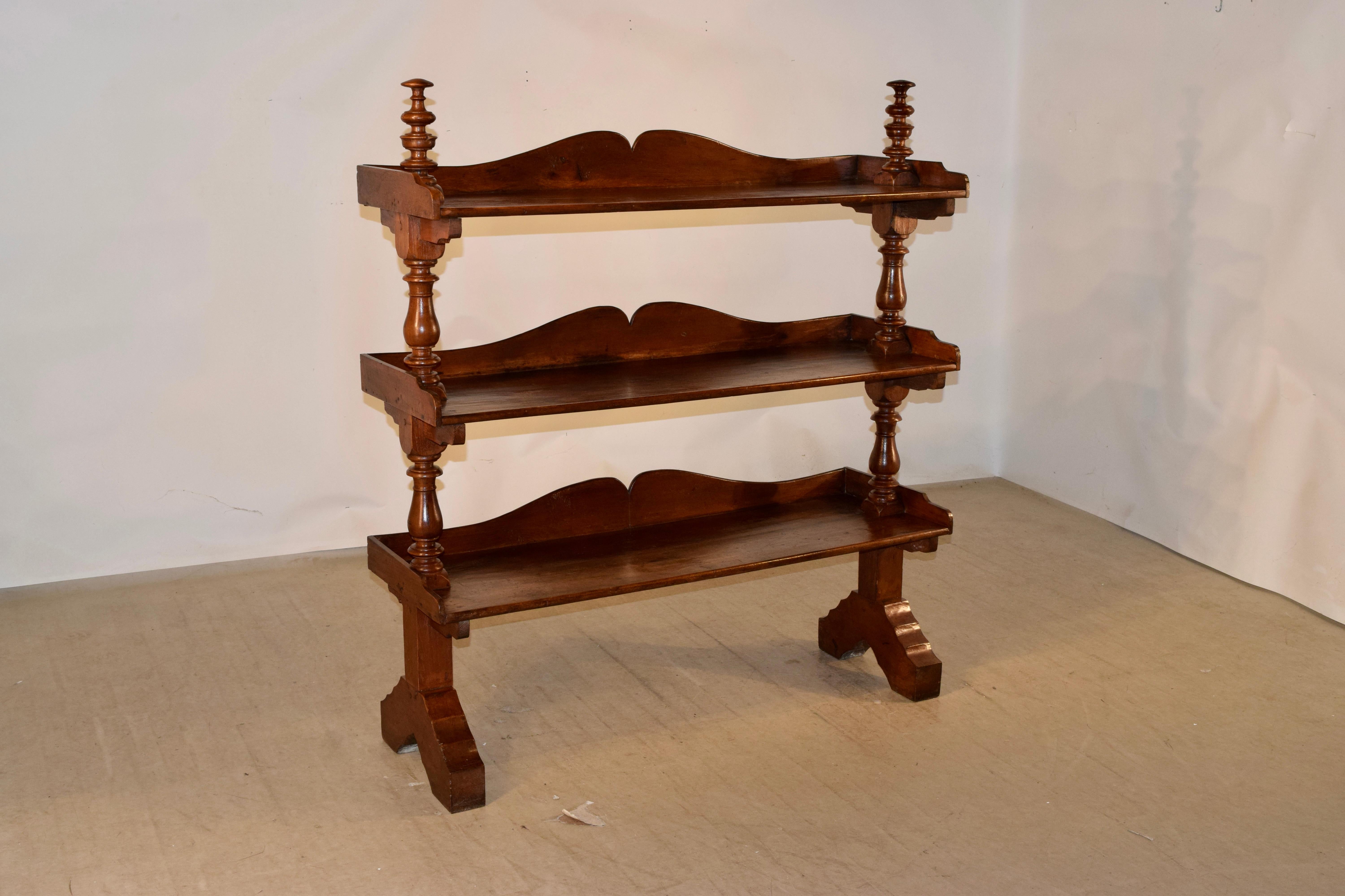 19th century British Colonial shelf made from teak. There are tall hand turned finials on the top over three shelves, all with scalloped galleries. The shelves are separated by hand turned shelf supports and the legs are shaped and splayed.