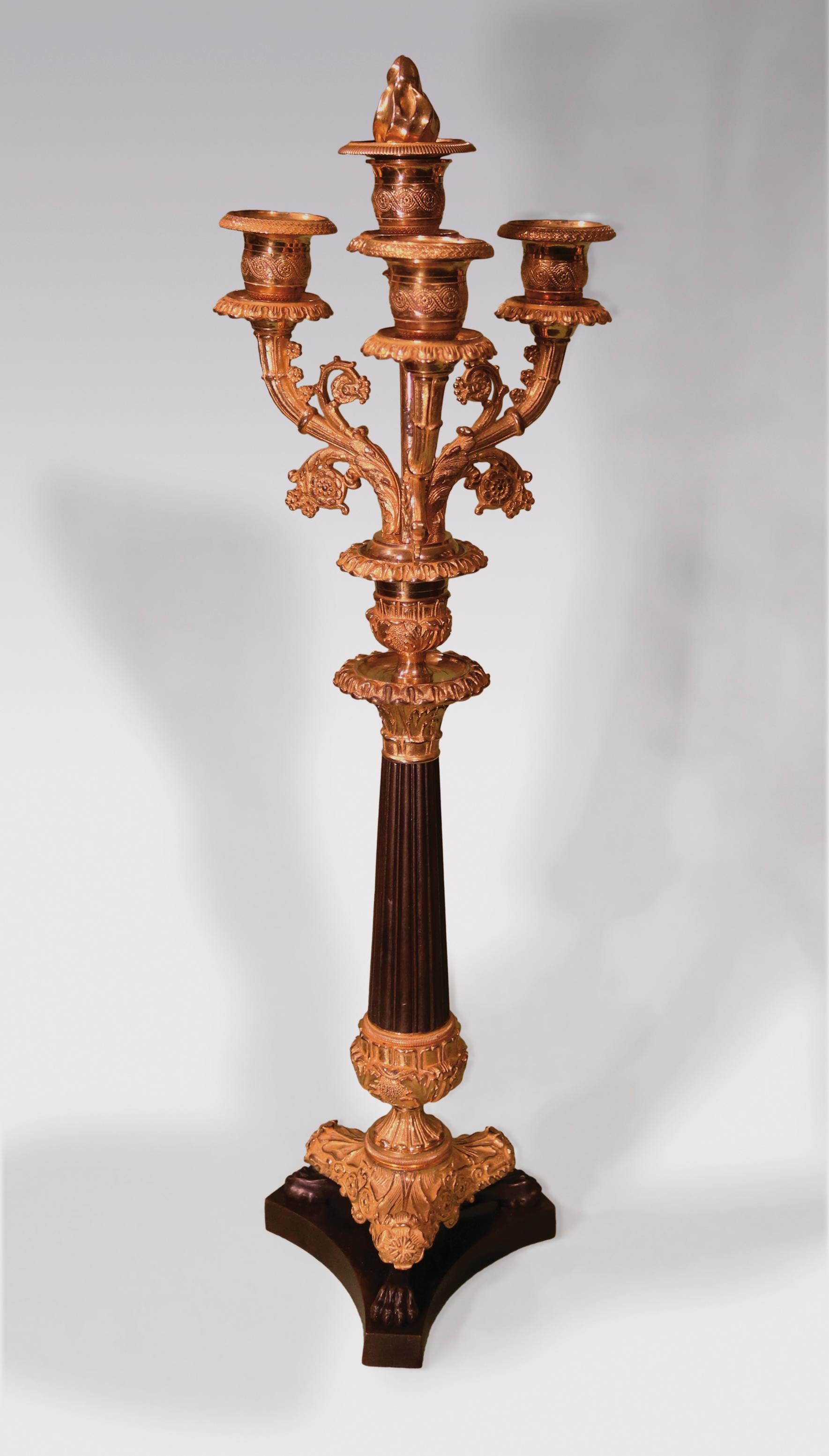 A pair of early 19th century bronze and ormolu 4-light candelabras with central finials, having leaf and spiral decorated nozzles raised on scrolled cornucopiae supported on reeded, tapering stems with lion’s paw feet ending on concave tri-form