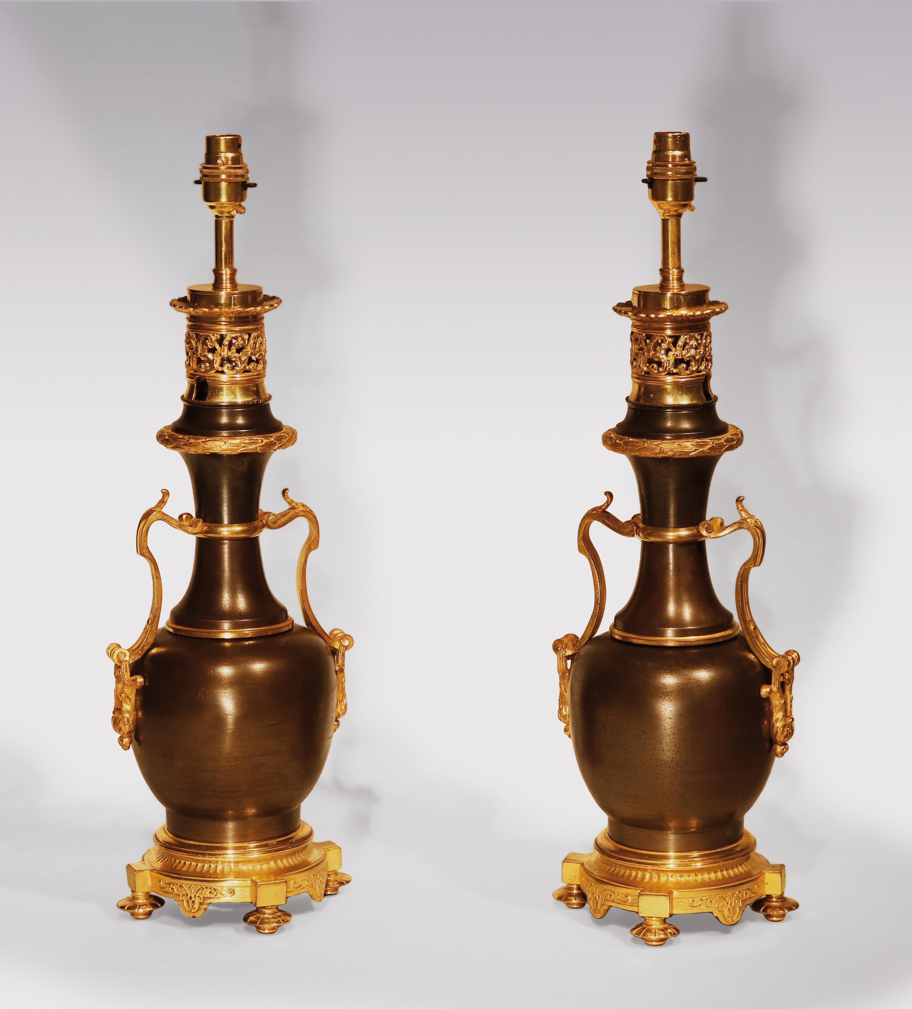A pair of mid-19th century bronze and ormolu oil Lamps in the form of bulbous shaped vases with scrolled carrying handles, ending on circular bases supported on turned petal feet.
(Now converted to lamps).