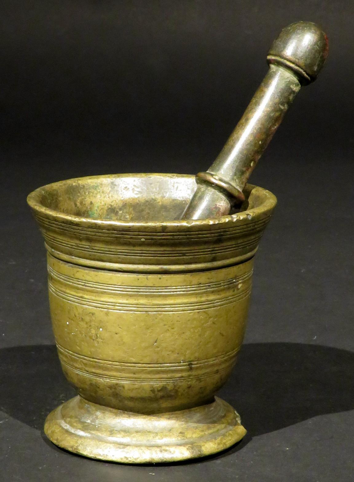 The cup shaped cast body decorated with incised ring-turned detail, rising from a waisted & stepped circular foot, together with its original pestle.
Combined weight, 3.75 lbs.
 