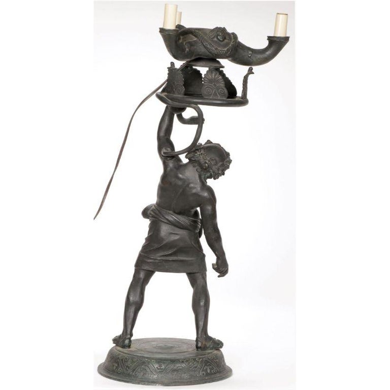 A bronze figural lamp of Bacchus holding a snake with a ring base carrying a three-light candelabra. Naples circa 1890. Height 26 inches (66 cm).