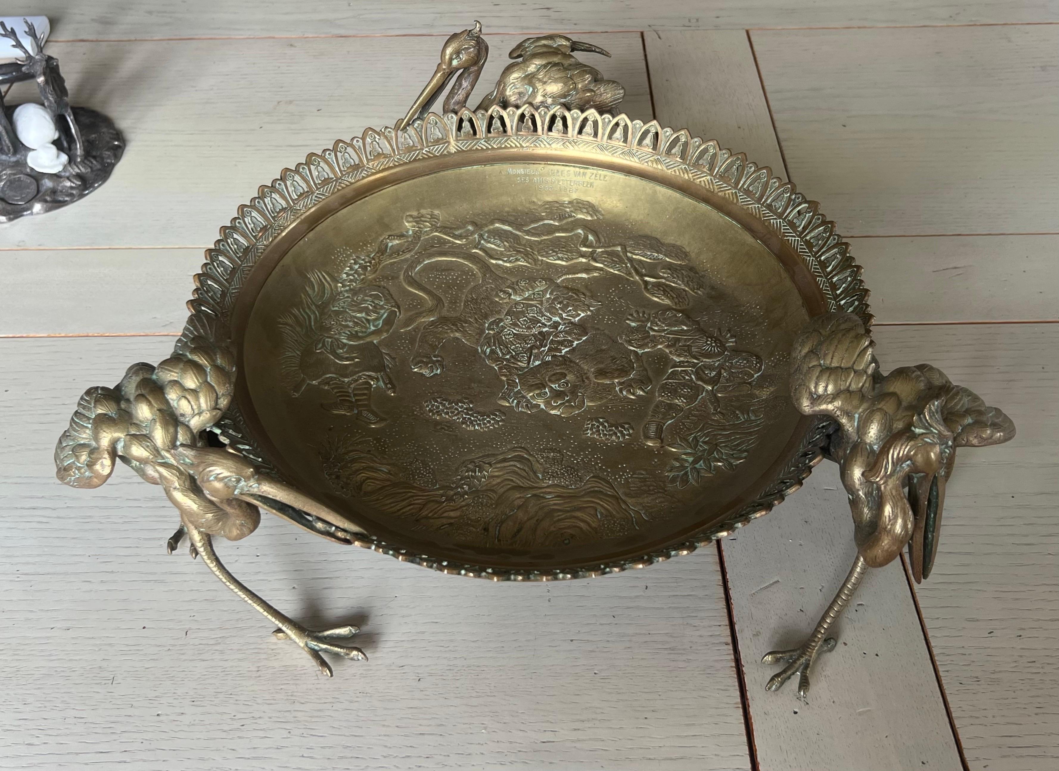 Centre de table rond en bronze asiatique gravé à la main, décoré d'un puissant tigre entouré de trois figures d'hommes en costumes traditionnels. L'objet est tenu par trois grues dans des postures différentes. Une dédicace gravée est apposée sur la