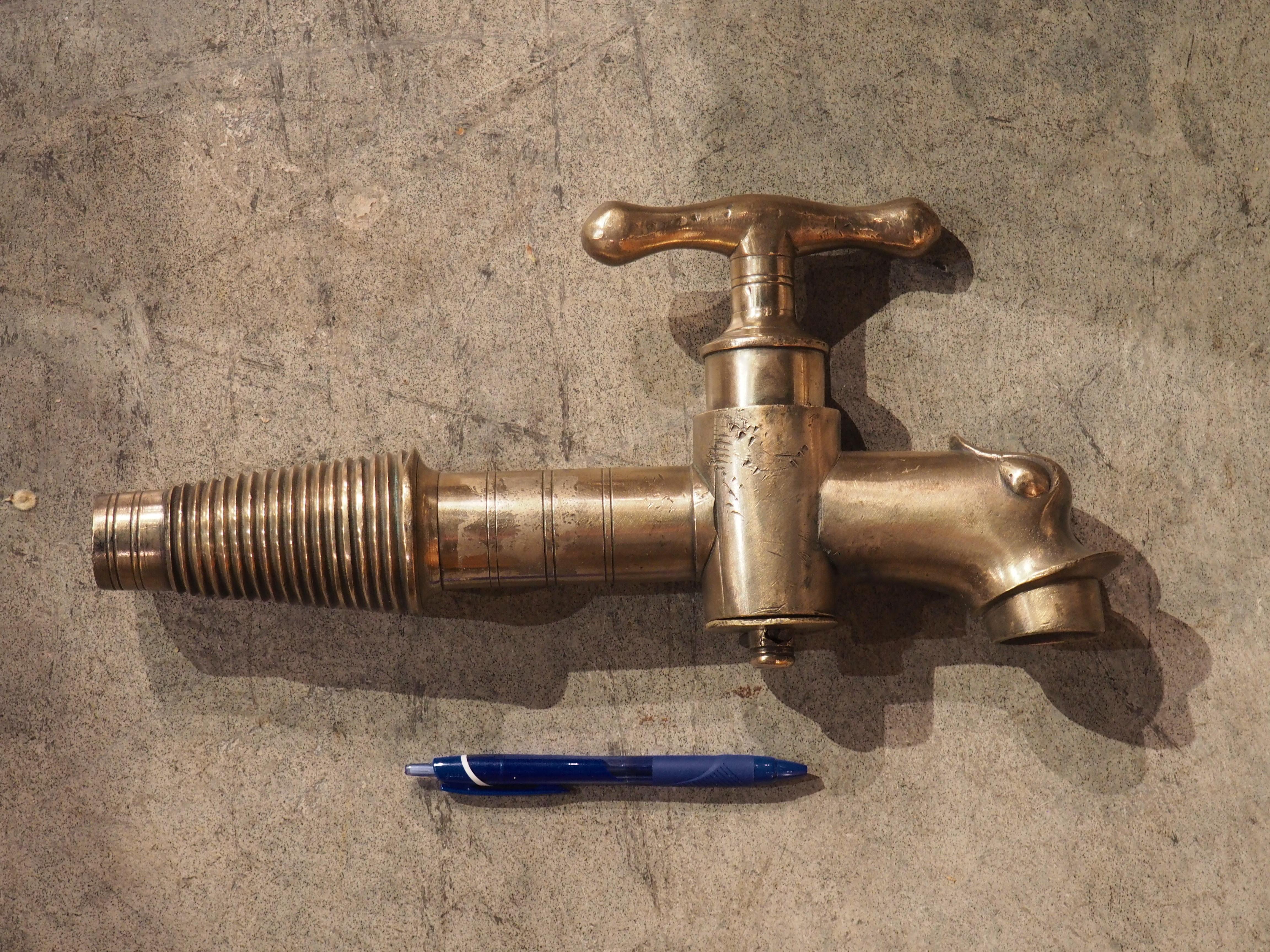 This large bronze wine barrel spout was cast in the 1800s in France. The spout is in the form of a dolphin head, with the mouth functioning as the exit point. A large, shaped handle emerges from the top of a tapering and threaded stem. Our dolphin