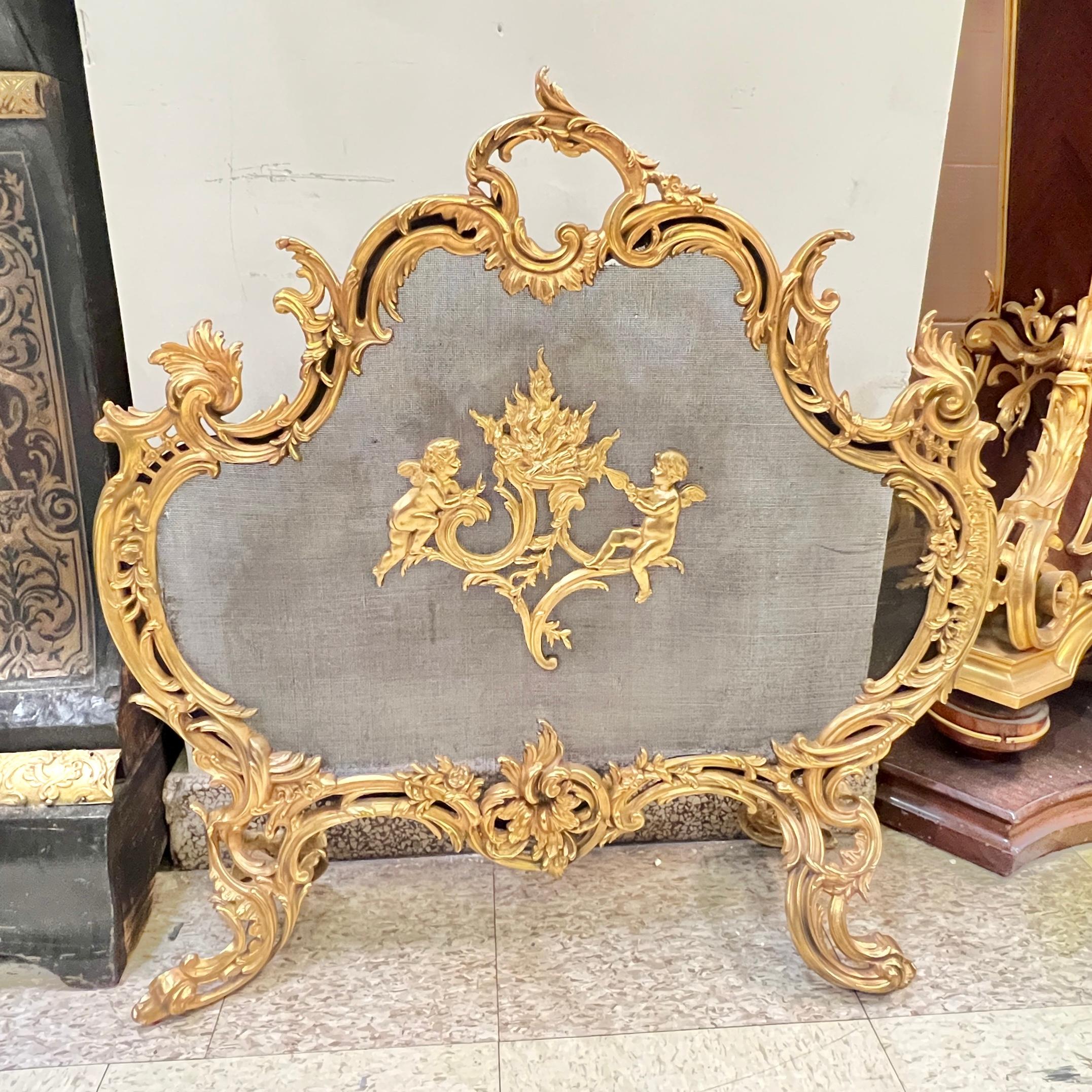 Antique (19th century) gilt bronze fireplace screen in the French Louis XV / XVI style, featuring cherubs tending to a flame and frame with organic motifs including connected scrolls and rocaille.  29 inches wide, 28 1/2 in tall and 9 in deep.