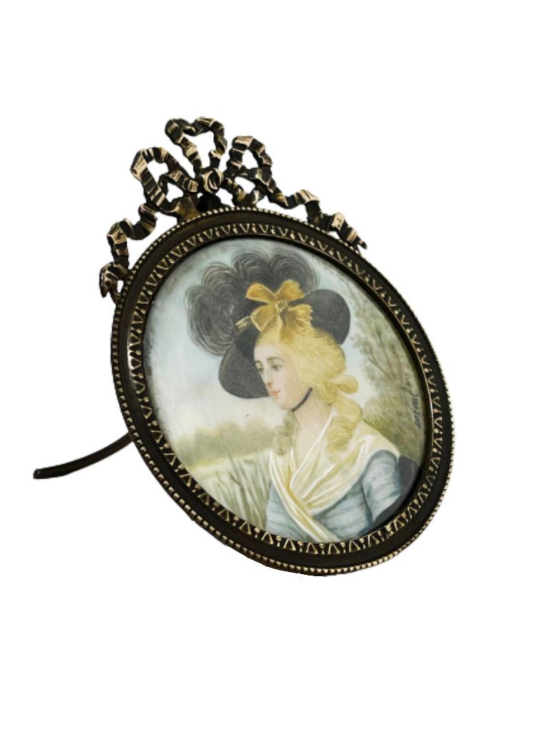 A 19th century bronze miniature portrait frame by Jean Derval

A French hand-painted portrait of a lady, probably Miss Viddom in a bronze frame, behind convex glass. Crowned with a bow on the bronze frame. 
Signed Drivel at middle right
The