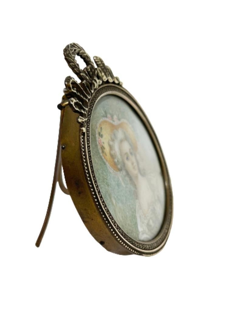 A 19th century bronze miniature portrait frame. 

A French oval hand-painted portrait of a lady in a bronze frame, behind convex glass. Crowned with laurel wreath and ribbon on the bronze frame. 
A bronze frame with stand and eyelet to hang
The