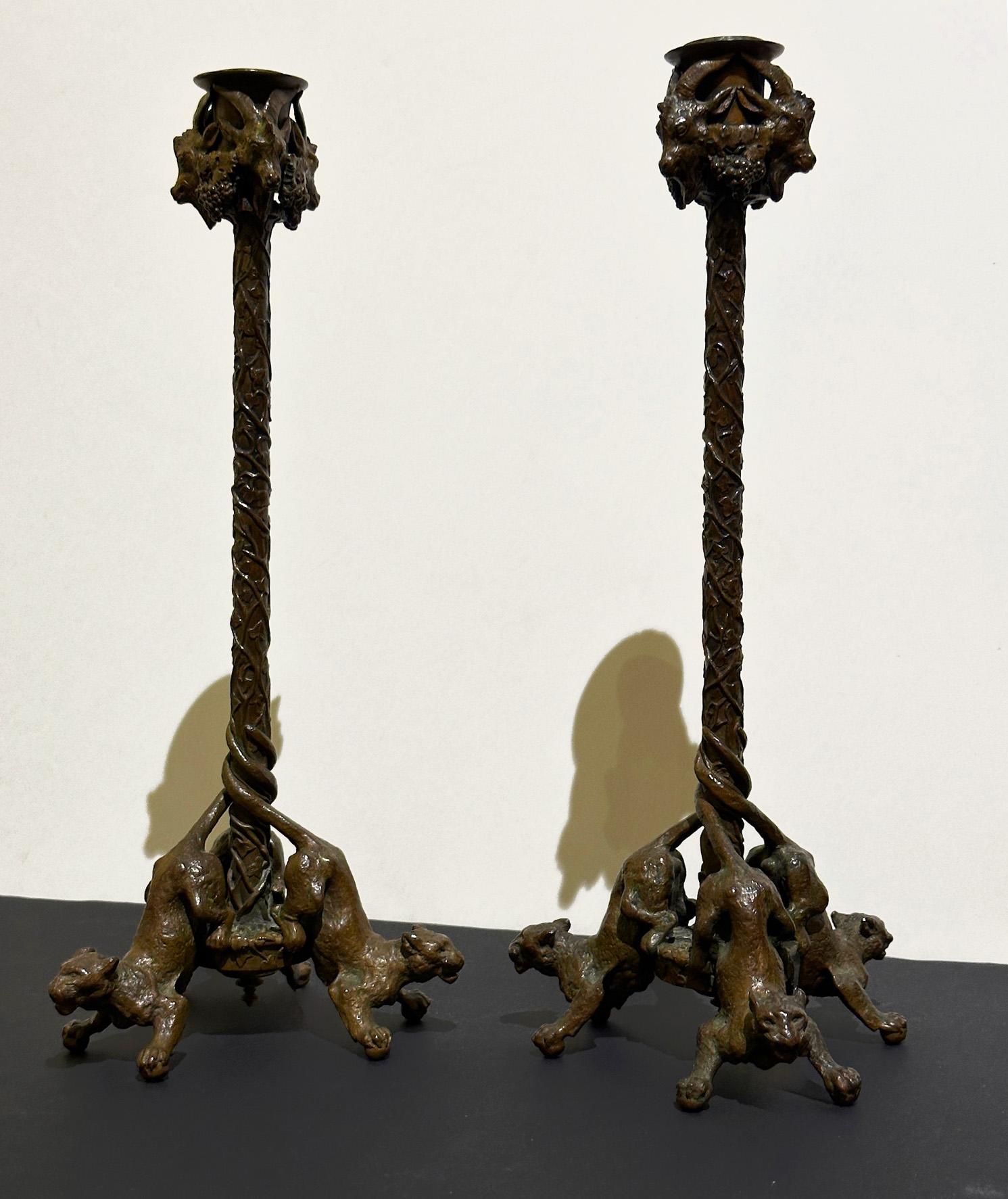 Here is a stunning pair of finely chiseled, bronze candlesticks from the mid-19th century. Each candlestick features ram's heads and grape clusters on the binet, while the shaft is adorned with leafy patterns and vines. The base is supported by
