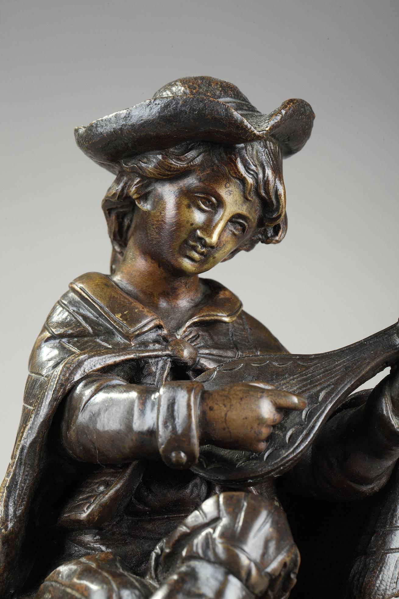 Small patinated bronze sculpture featuring a young boy sitting on a rock and playing the mandolin. He is wearing an elegant hat and his shoulders are covered by a cape. He evokes the Pifferari, Italian street musicians largely represented by the