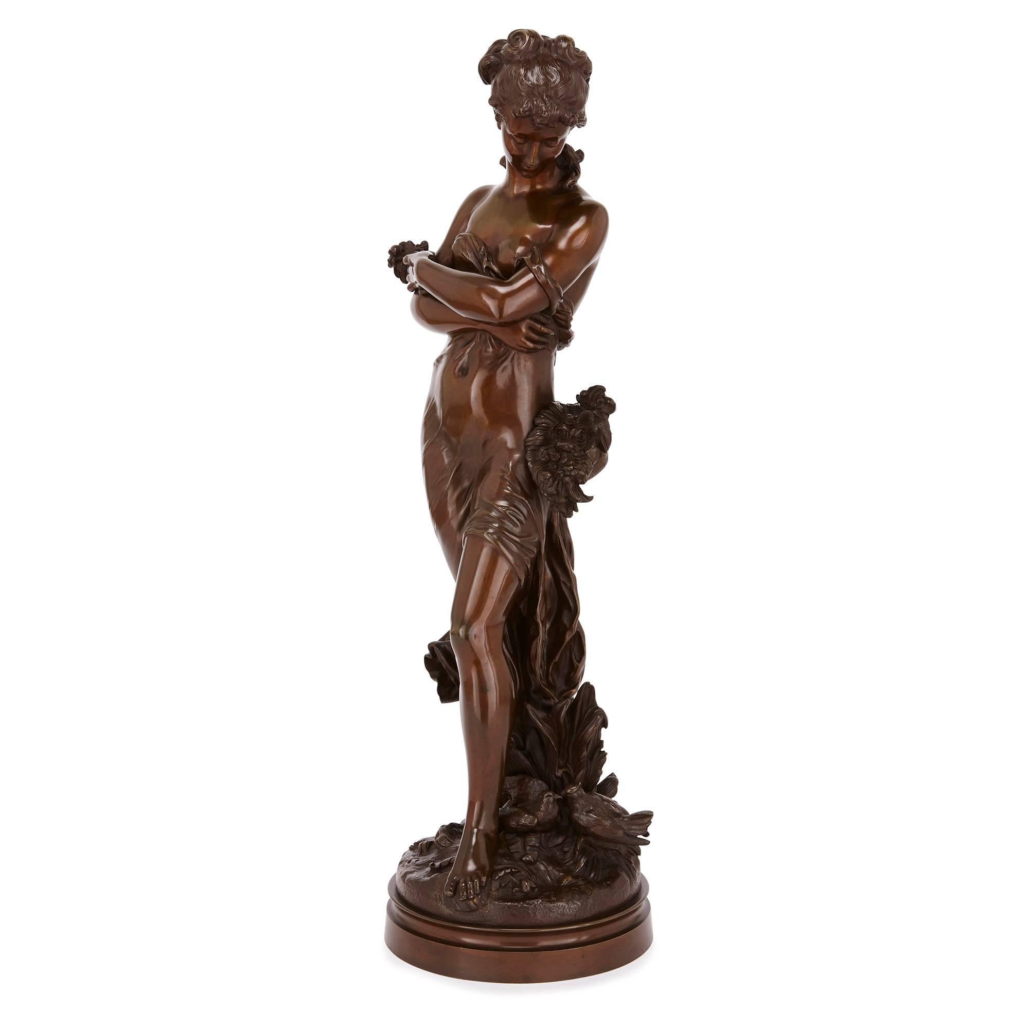 This alluring bronze depicts the full-length figure of a young lady who, swathed in draped clothing, looks downward toward a basket of flowers hung about her waist. The circular base upon which she stands is naturalistically cast as a forest