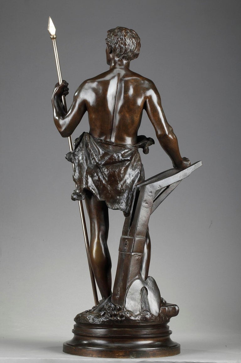 Bronze sculpture with brown patina by Ernest Rancoulet featuring an allegory of work with a young man holding a spear, that symbolizes the triumph of wisdom acquired through work and study. At his feet, several objects refer to literature, arts and