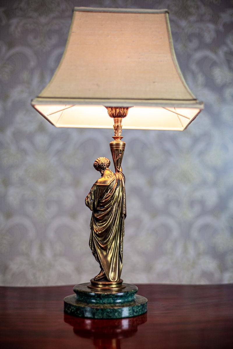 We present you this item, circa the 19th century, with a bronze base in the form of a statue.
There is a socket for a single E27 light bulb.
The power source is 230 V.

Dimensions of the lamp shade – H 27 cm, diameter at the base: 36 cm,