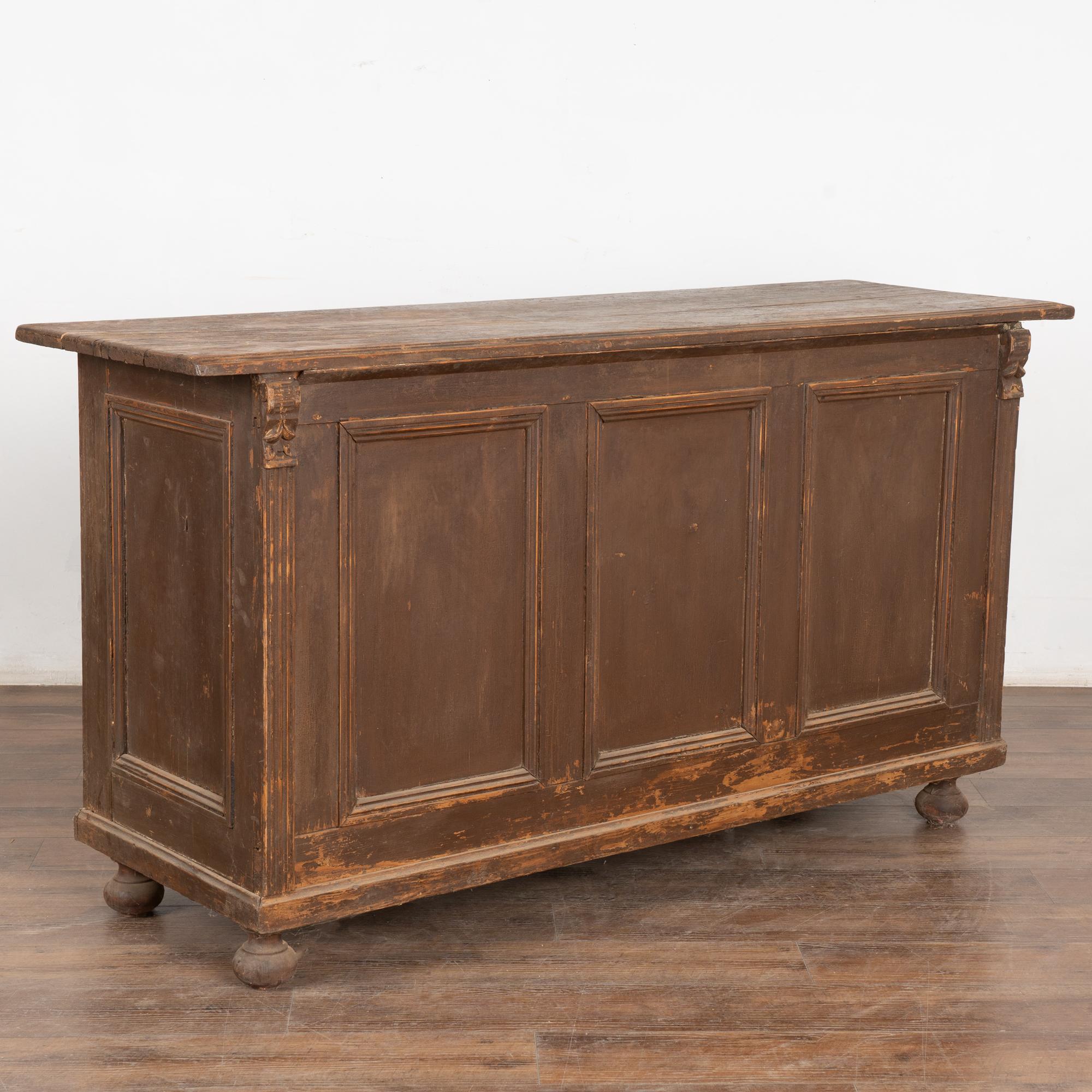 Antique shop counter with two large sliding cabinet doors, original brown paint over natural pine raised on bun feet. 
The back is paneled which makes this cabinet ideal for a free standing kitchen island, but may also be used as a cabinet, console,
