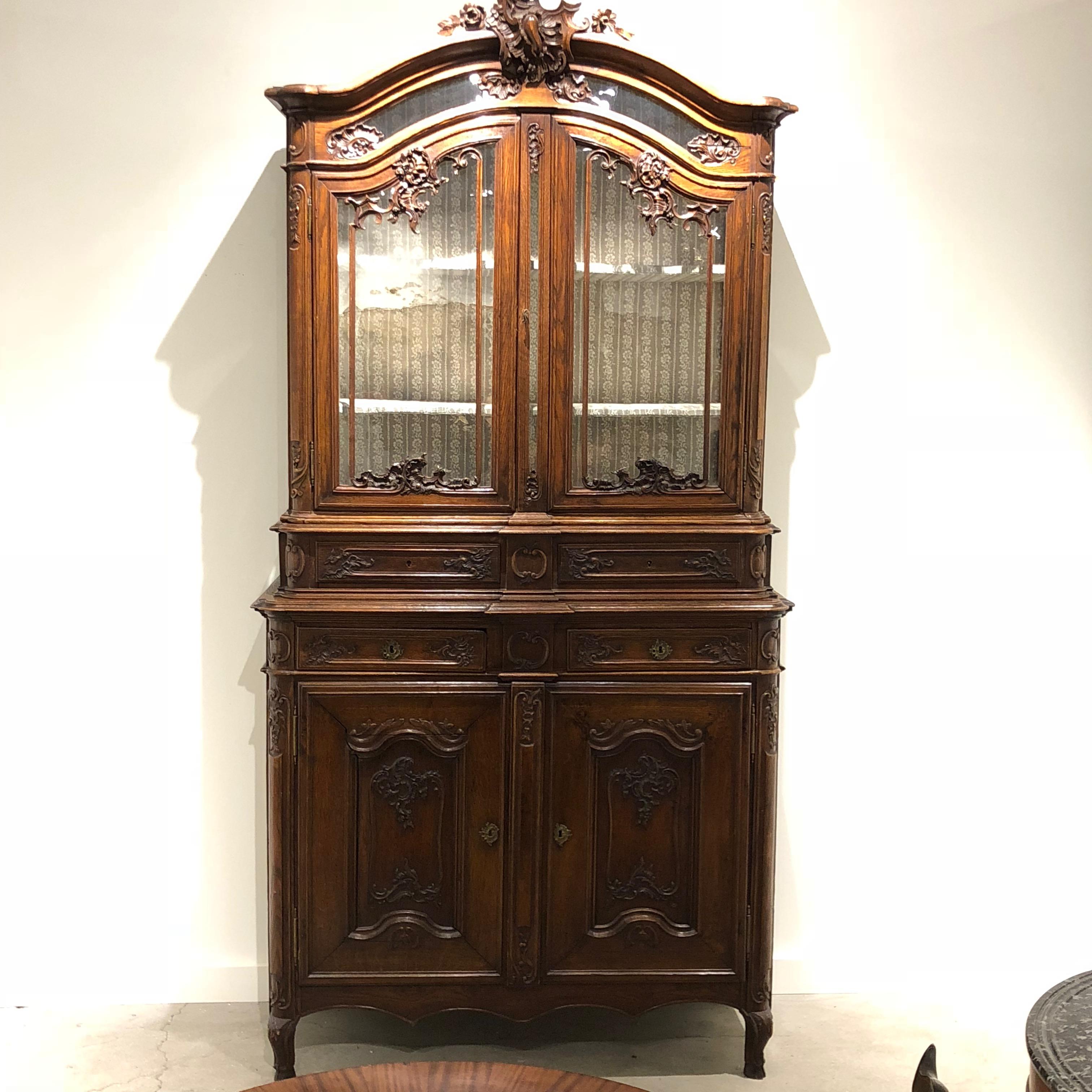 An elegant buffet deux corps with two doors that lock with a key, four small drawers that open in the centre and two glass doors that open with the turn of a small latch. Detailed with decorative wood carvings throughout, a beautiful carved crest