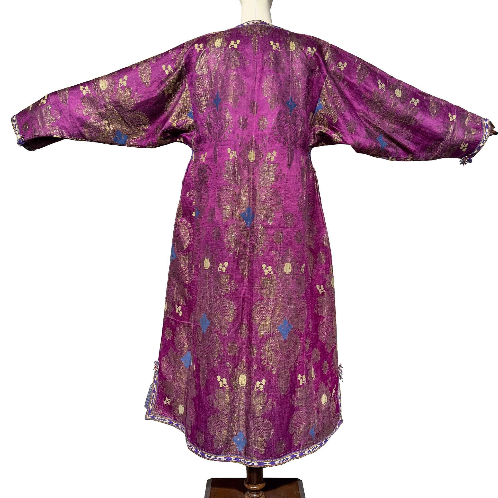 Cette élégante robe de femme est confectionnée en brocart de soie de Boukhara du milieu du XIXe siècle, tissé à l'origine pour les traditions textiles raffinées d'Asie centrale. La couche extérieure présente un fond fuchsia-pourpre lumineux orné