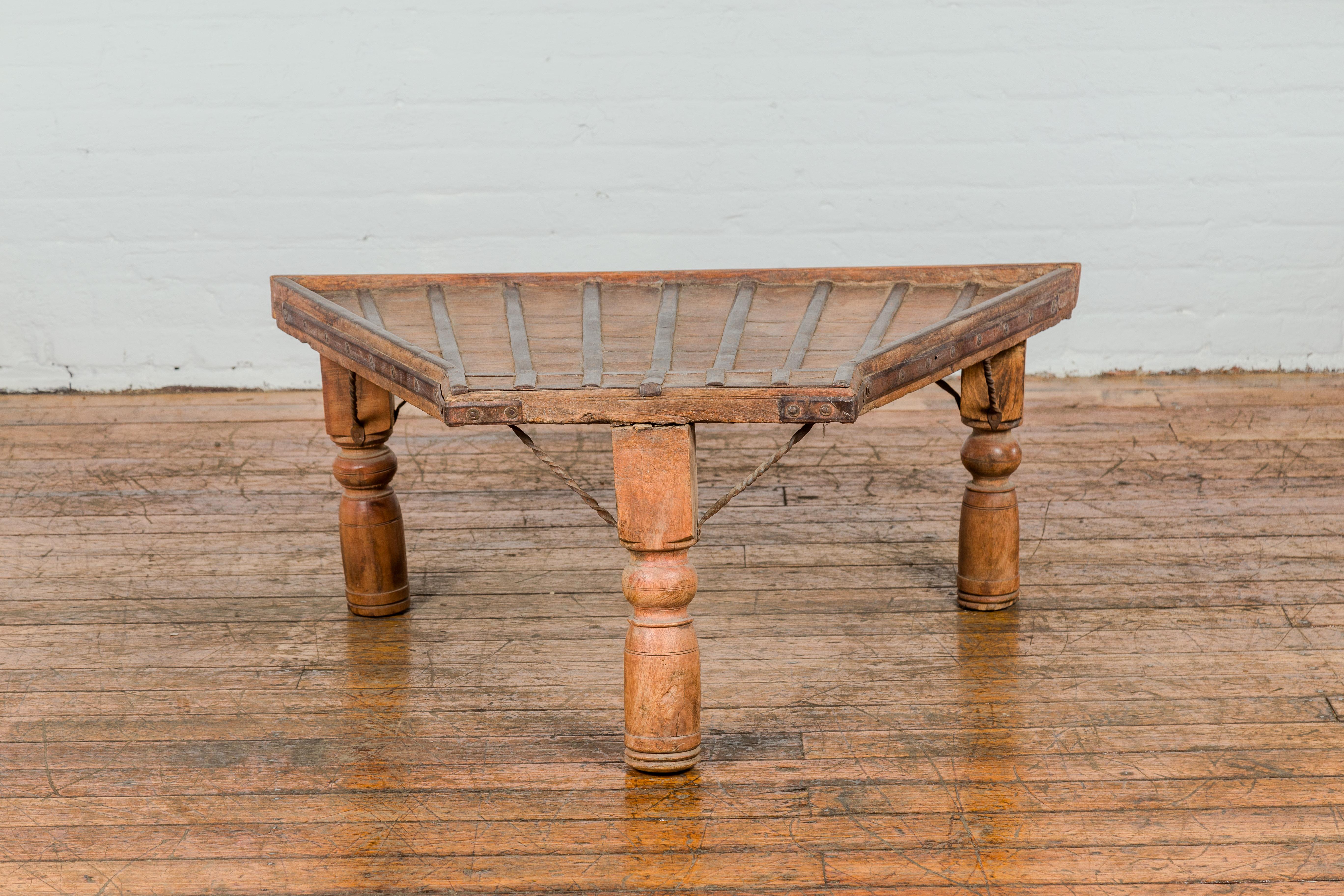 An antique rustic Indian handmade coffee table with trapezoidal top, protruding front, twisted iron stretchers, turned baluster legs and nicely weathered patina. This antique rustic Indian handmade coffee table, crafted from the front portions of a