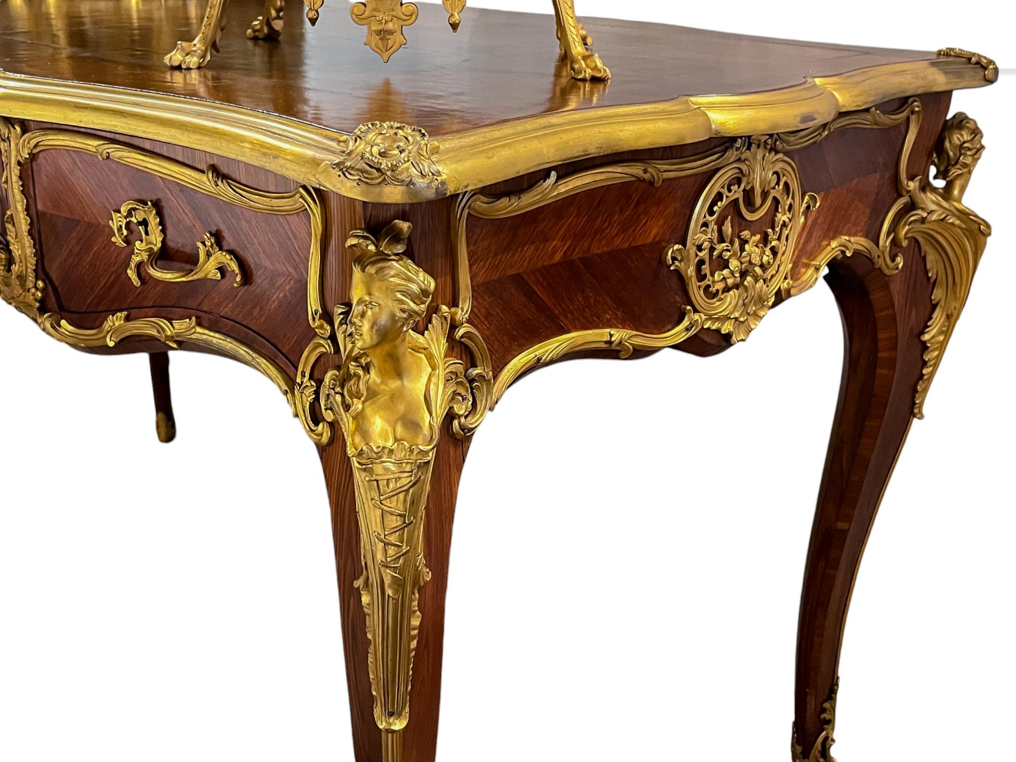 Un sublime Bureau Plat Desk in legno di Kingwood con nitide montature in ormolu in stile Luigi XV. Una serie di quattro cariatidi femminili orna ciascuna delle gambe ricurve, con scudi montati ai quattro angoli della scrivania, che incorniciano il