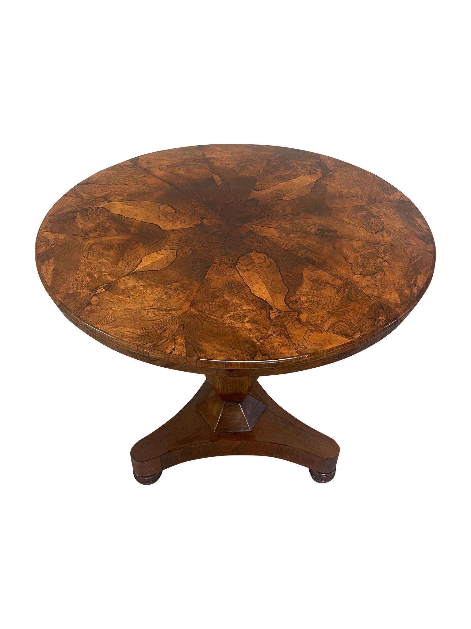This is a wonderful 19th century Pedestal Table, crafted in walnut and burled walnut veneer. Characterized by its rounded top, apron drop feature, and tripod plinth with working hard wood casters, the burled veneer creates an organic and captivating