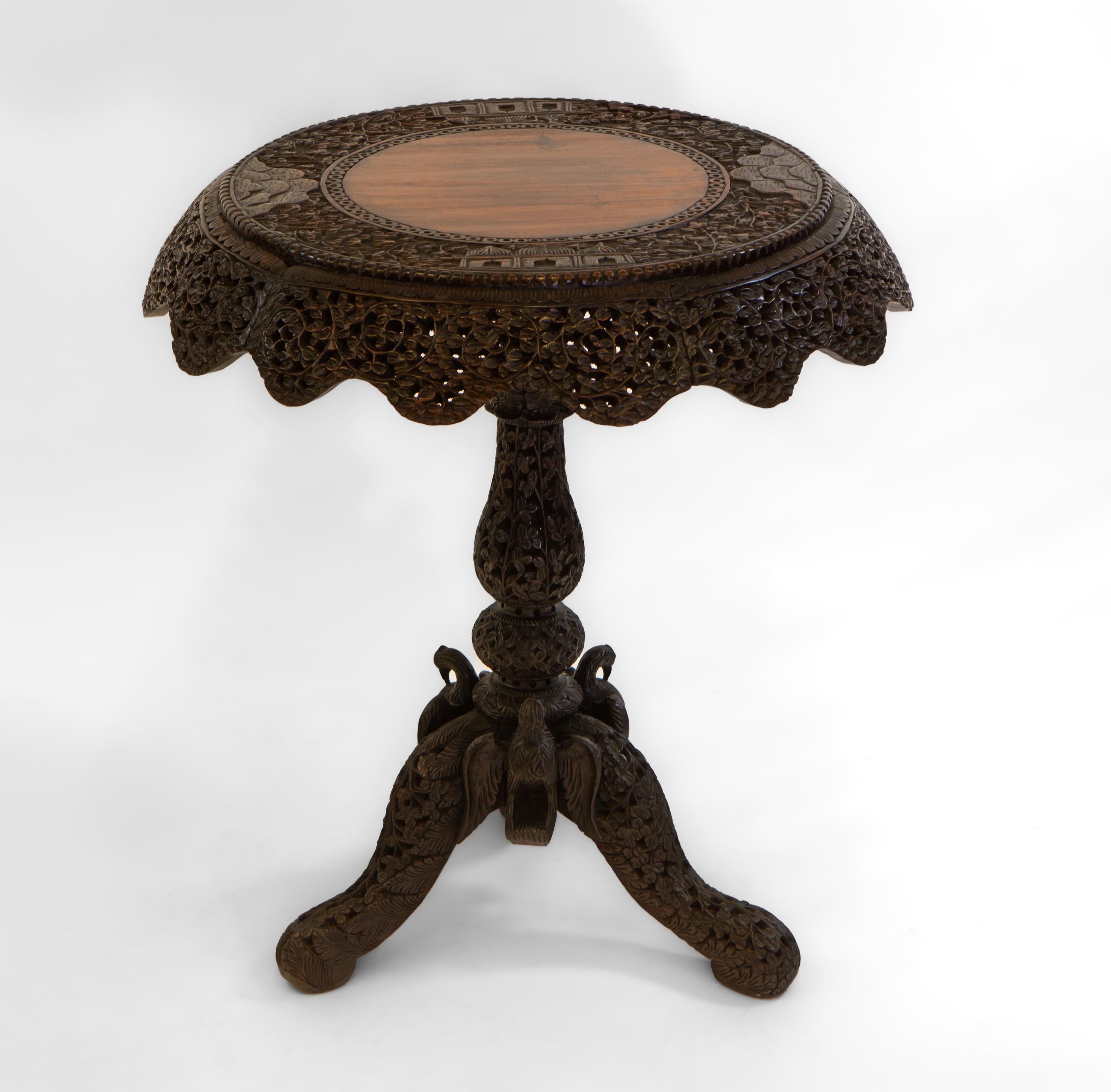 Magnifique table d'appoint ancienne en bois de padouk birman (aujourd'hui Myanmar) abondamment sculpté à la main. Circa 1880.

Le plateau de la table est orné d'une bordure décorative avec une frise en forme. La table est ornée d'un feuillage percé