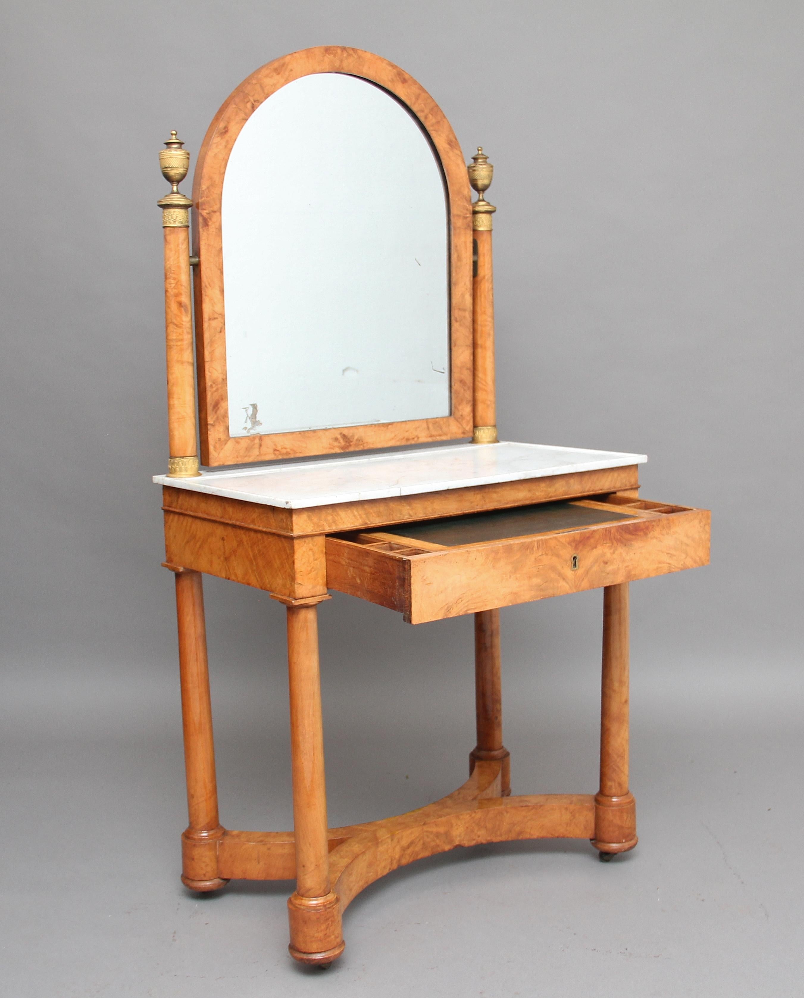 19th century French burr elm Biedermeier dressing table, standing on four turned columns united by an X-stretcher and terminating on four castors, a white marble top above a frieze drawer with a writing surface and compartments either side, above