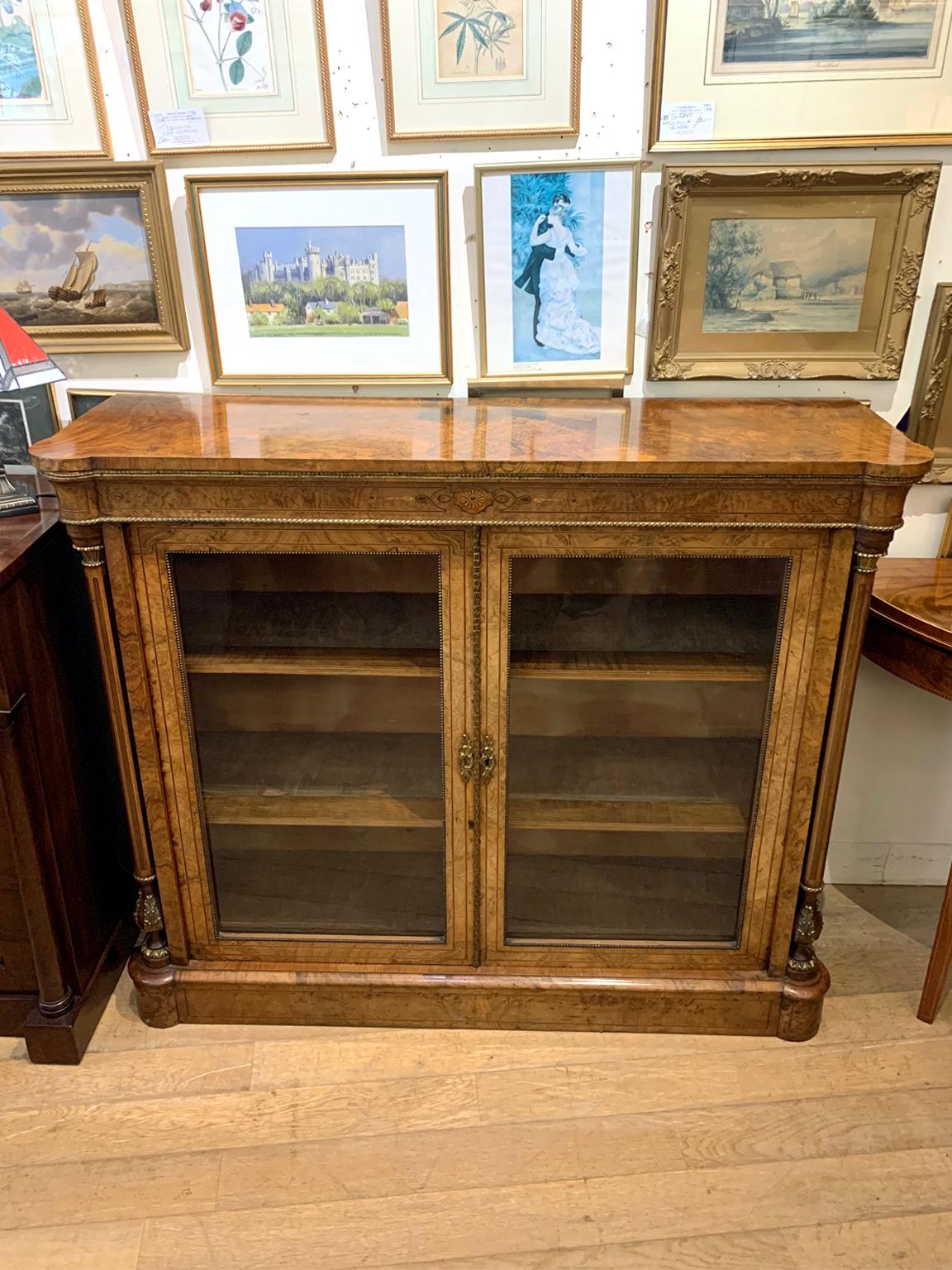 A very high quality 19th century burr walnut bookcase / cabinet with gilt metal mounts and marquetry inlaid decoration throughout, glazed doors enclosing original fitted shelves flanked by inlaid columns, on plinth base.

Circa: