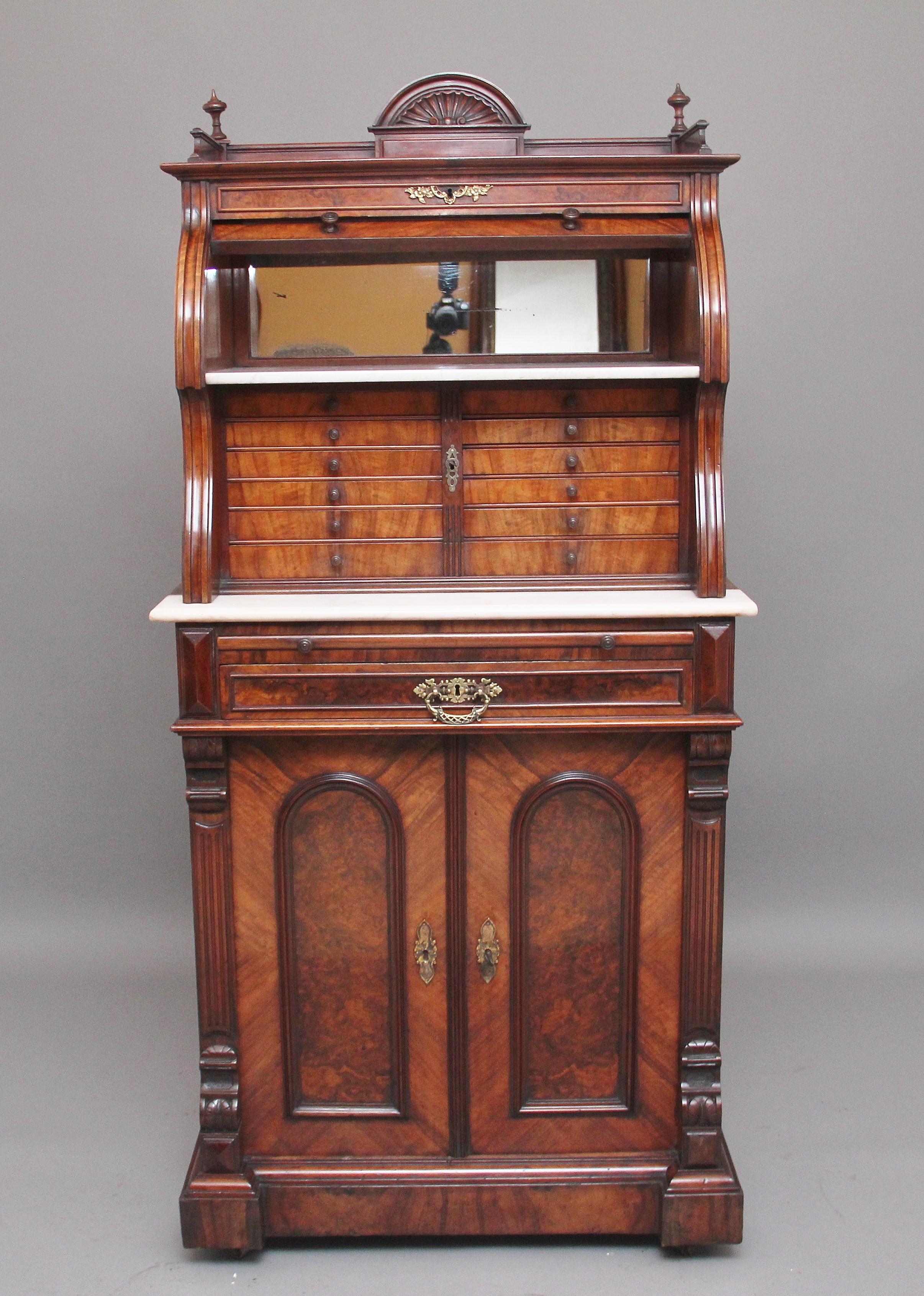 19th century burr walnut dentist cabinet, the top section having a carved shell top gallery with decorative finials either side, the cylinder opening to reveal a mirror and white marble, twelve graduated burr walnut drawers with original turned