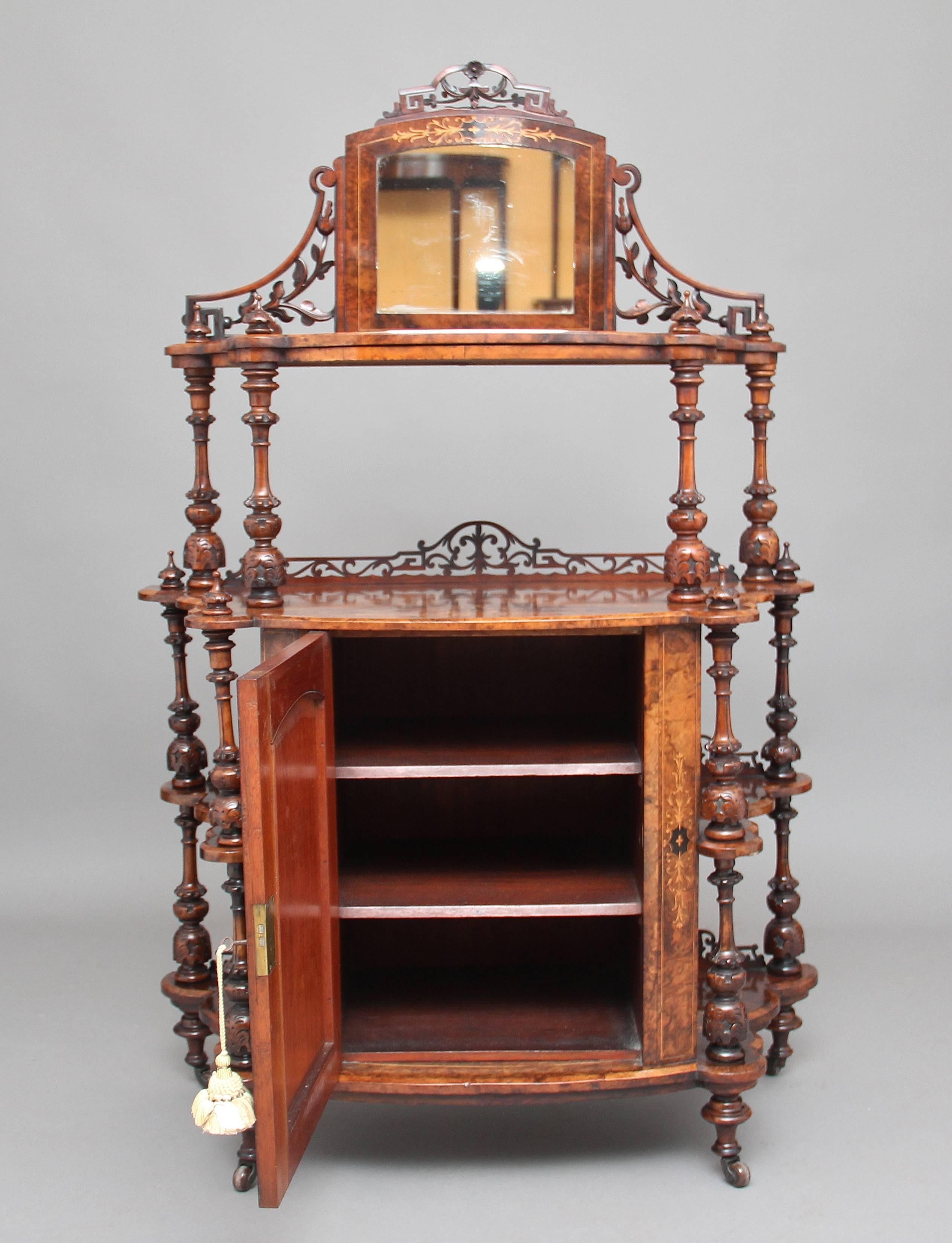 19th century burr walnut and inlaid whatnot cabinet of bowfronted form, having a fret carved mirrored superstructure above a shelf supported by carved and turned columns finishing with carved finials, a single door below opening to reveal two fixed
