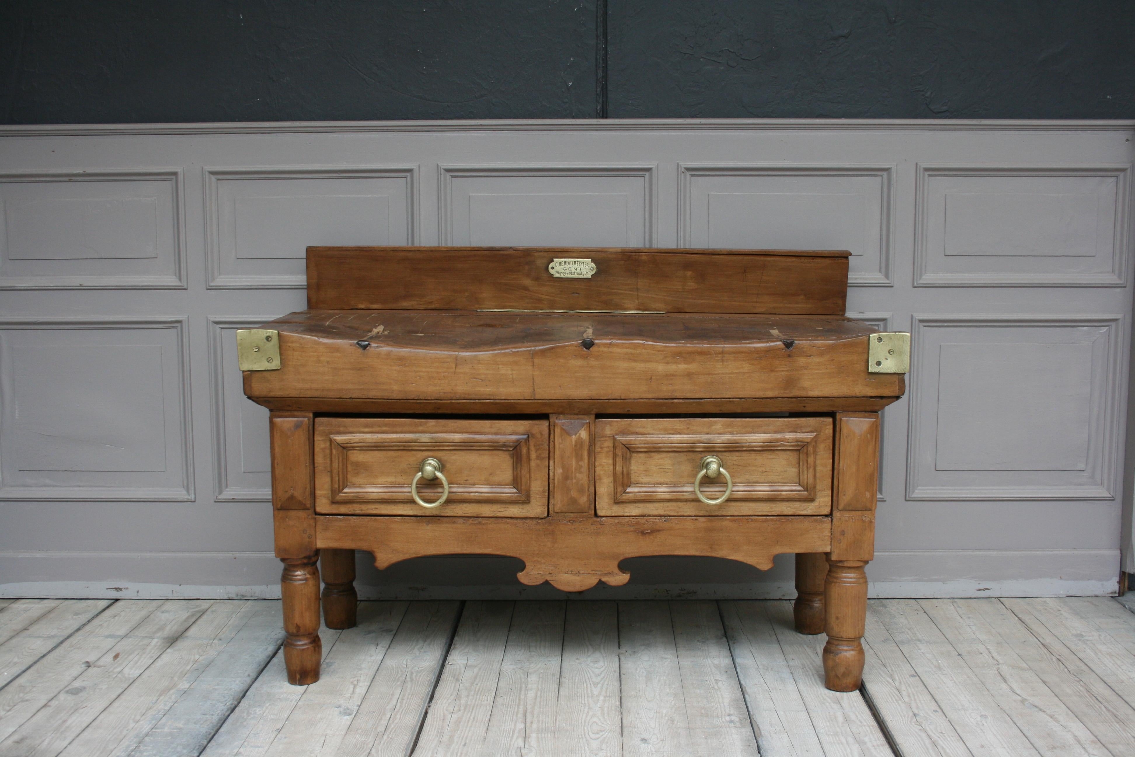 A large late 19th century butcher block table from Belgium. Standing on 4 massive turned feet with manufacturer's badge, brass or bronze fittings and 2 drawers. 

Dimensions: 
80 or 95 cm (including the backboard) high / 31.5 or 37.4 (including the