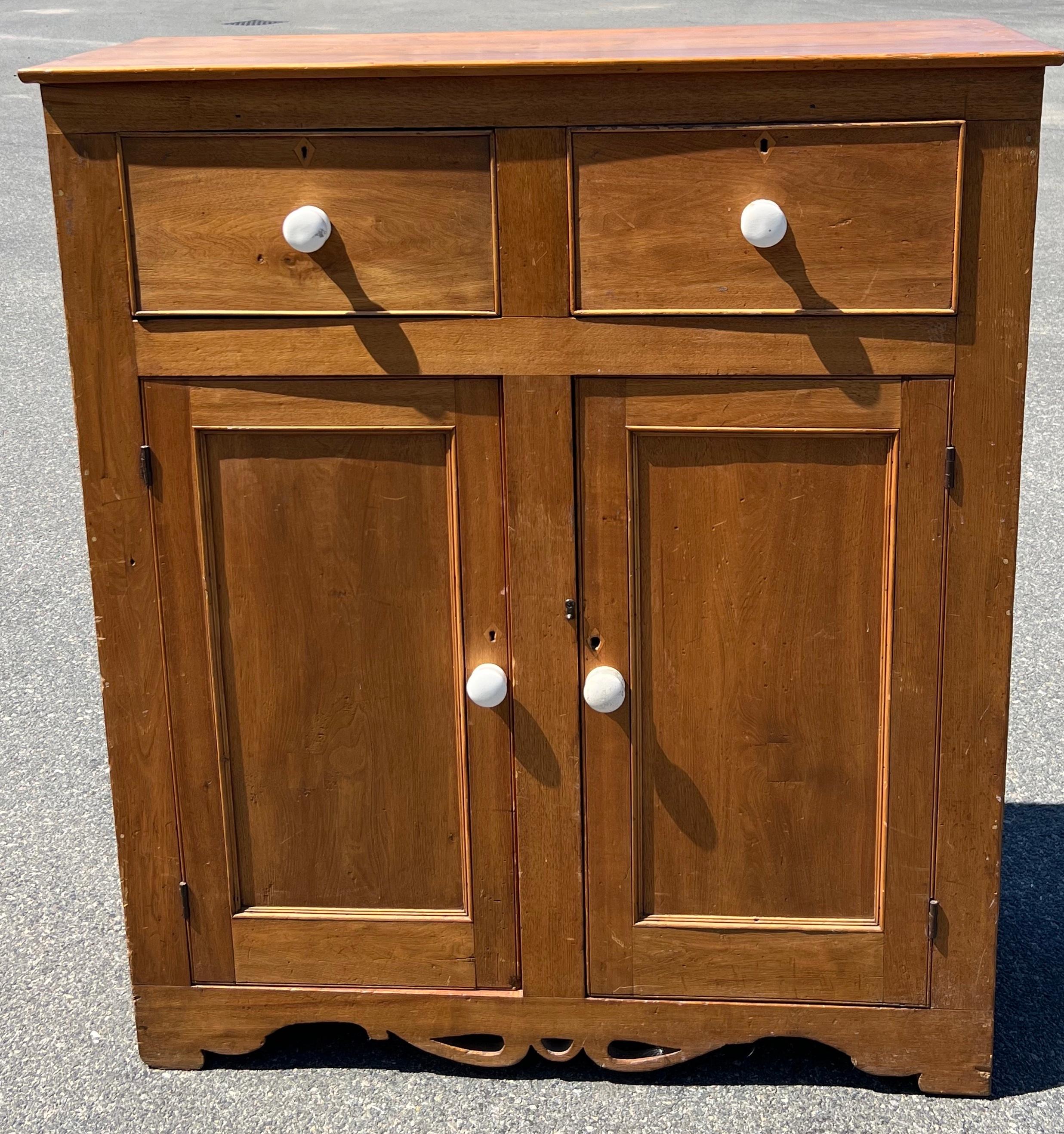 19th Century Tall Butternut Cupboard with white porcelain knobs.  Two beaded drawers over two paneled doors, diamond inlaid keyhole details (no keys), delicately shaped toe kick with cut-outs.
