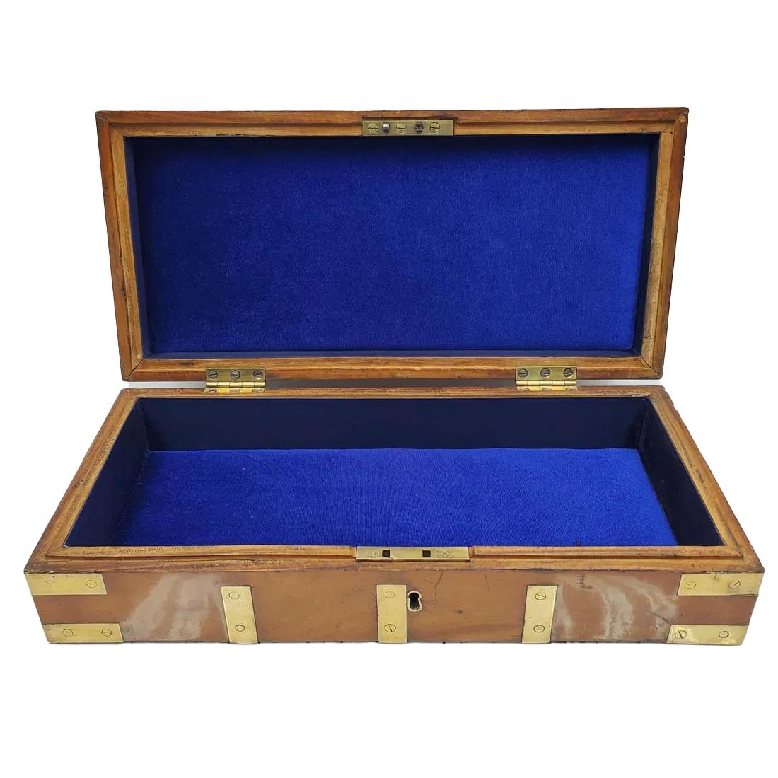 Custodia in legno di canfora montata in ottone, probabilmente per strumenti, di forma allungata e piatta con coperchio a cassettoni con angoli e cinghie in ottone. Il coperchio e le due estremità sono dotati di maniglie montate a filo, con serratura