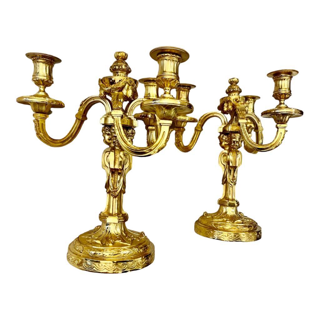 A stunning pair of directoire Louis XVI-style gilt bronze candlesticks with three lights, embellished with adorable acanthus leaf-topped putti figures adorning their stems. These candlesticks boast a broad, finely chiselled plate and display a
