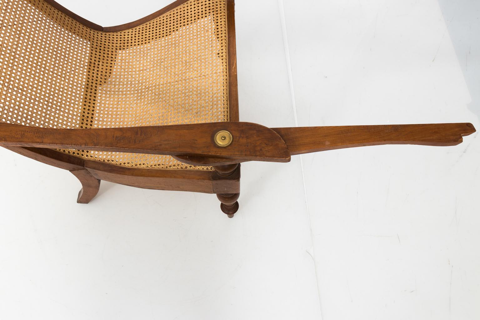 19th century chic and comfortable teak plantation chair with caned seat and backrest. Robust turned legs and swing-out arm for resting legs, embellished with unusual brass hardware detail.
  
