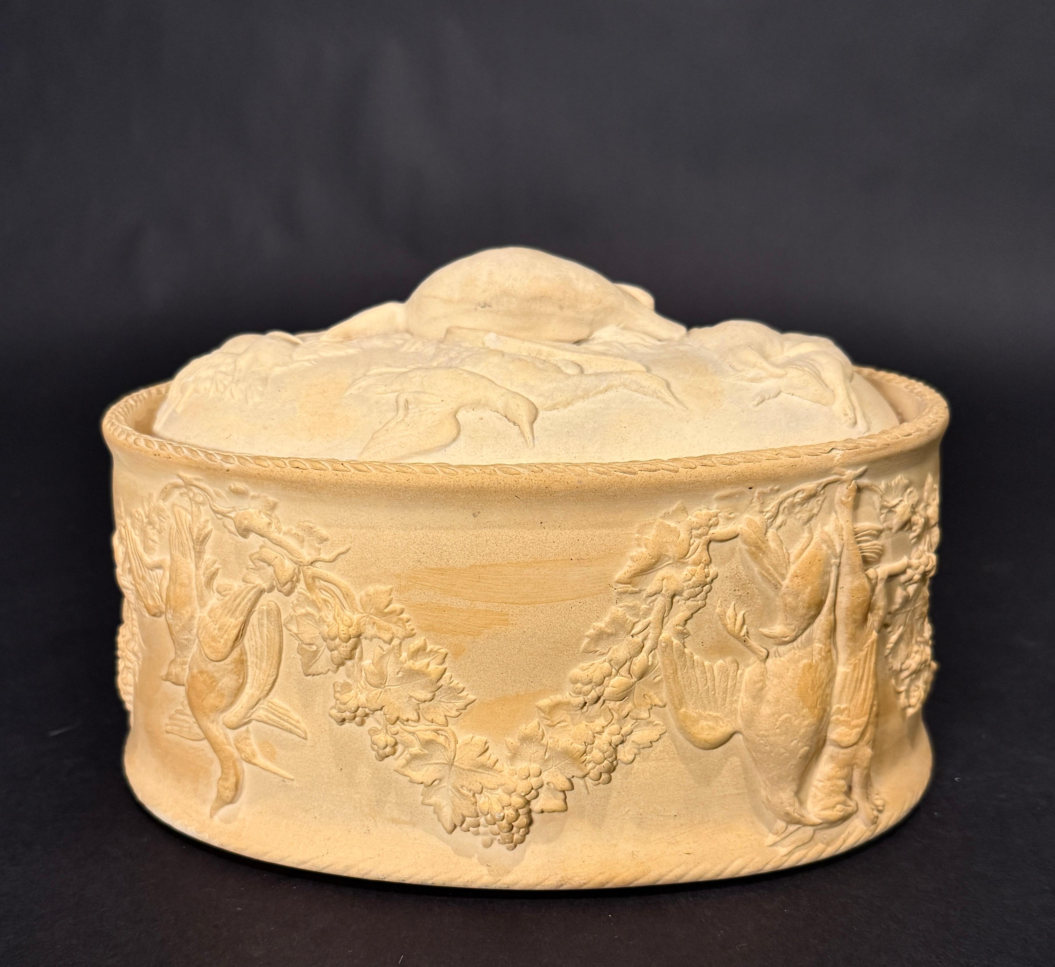 Plat de service ovale en céramique du milieu du 19e siècle, probablement de Wedgwood, avec un extérieur non émaillé (pour ressembler à une croûte de tarte) et des images moulées en relief de gibier (canards et lièvres) au milieu de festons de vigne,