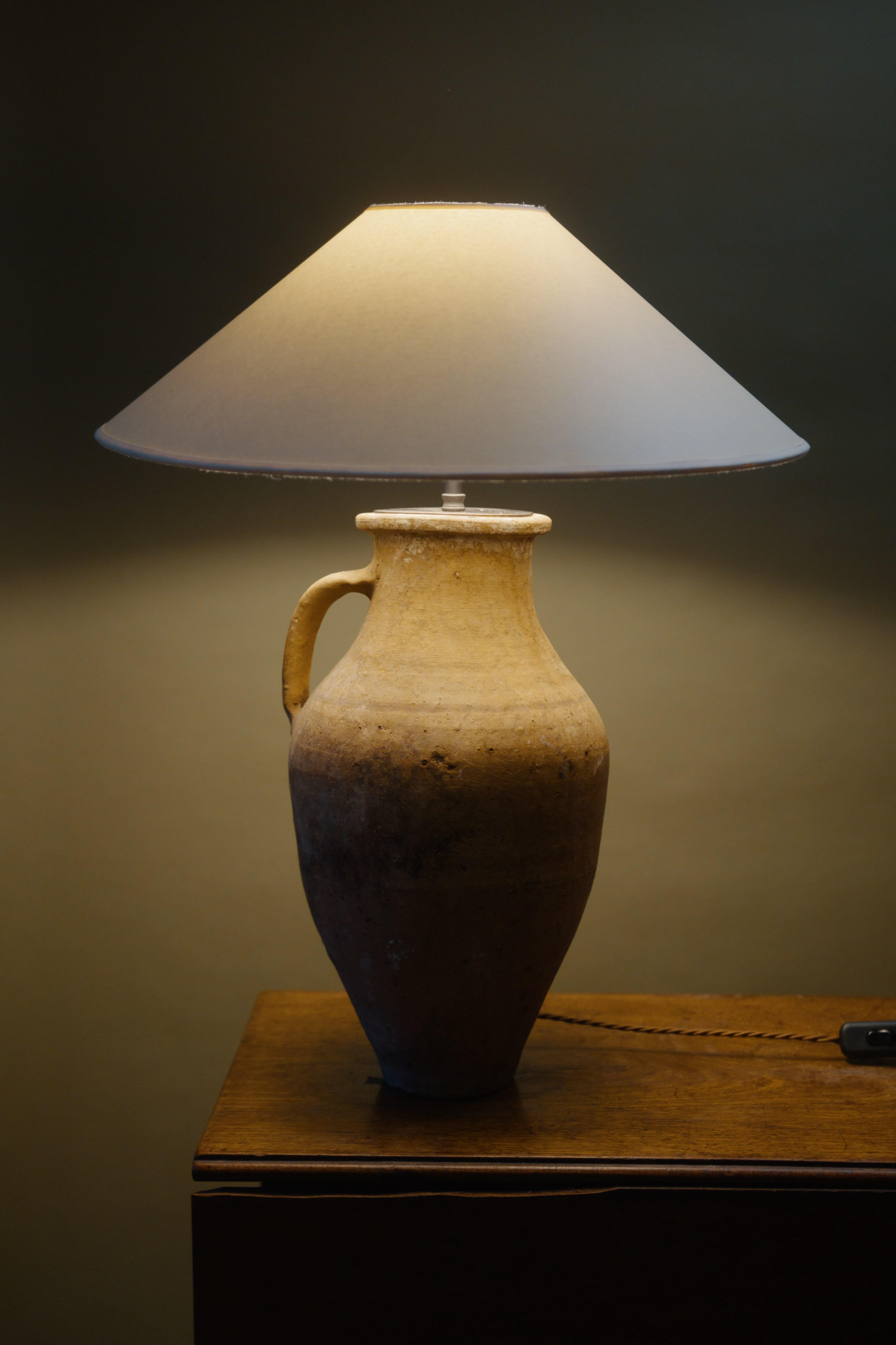 Cette lampe de table en amphore de la Cappadoce du 20e siècle est un exemple frappant de savoir-faire artisanal combiné à un design intemporel. Fabriqué à la main à partir d'un pot d'argile méditerranéen vintage, sa patine rustique ajoute de la