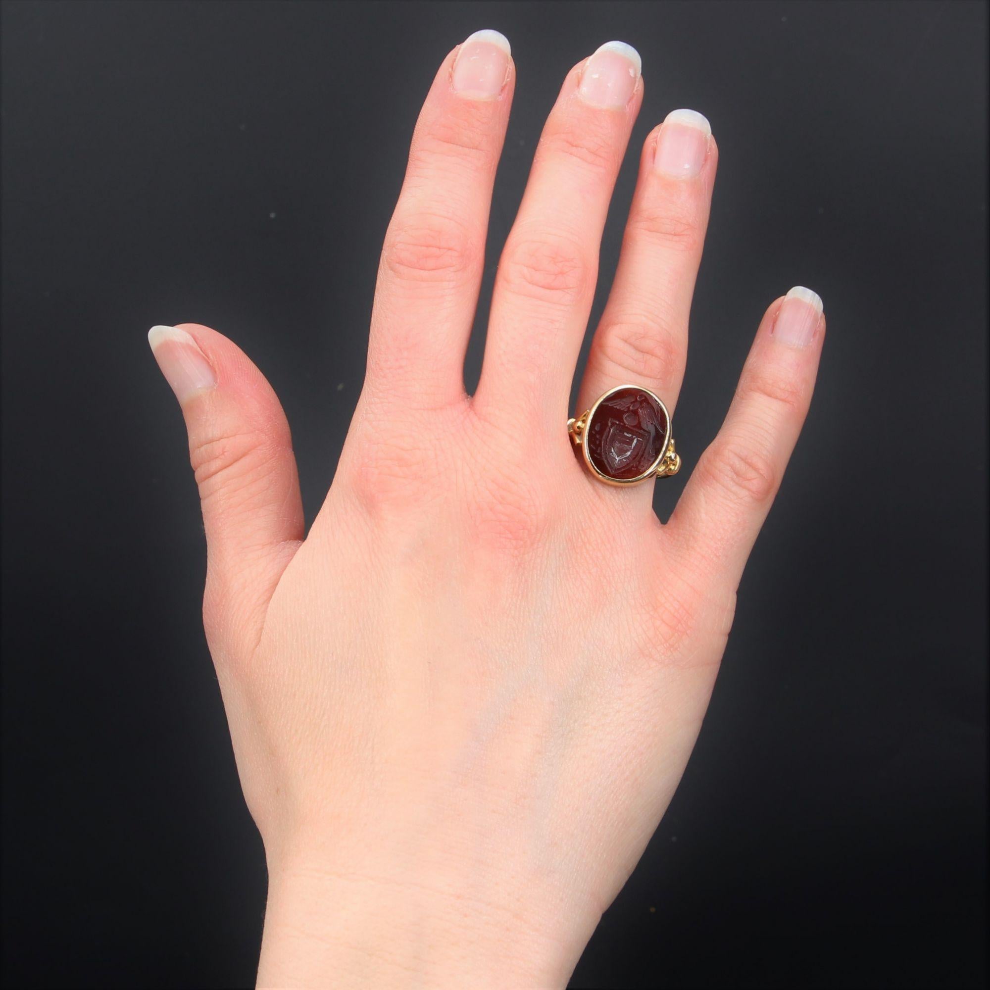 Ring in 18 karat yellow gold.
Elegant unisex ring, its top is an intaglio on carnelian representing a shield surmounted by an eagle and, on both sides, laurel leaves, all in closed setting. The start of the ring is a fork that holds a gold pearl and