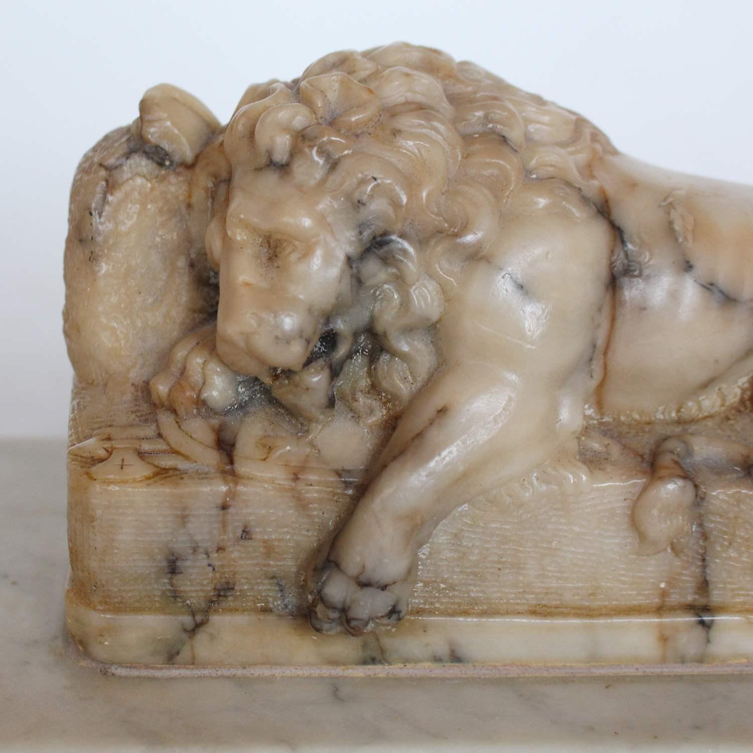 A 19th century carved alabaster lion lying on an integral plinth, set over a marble base. Unsigned.

