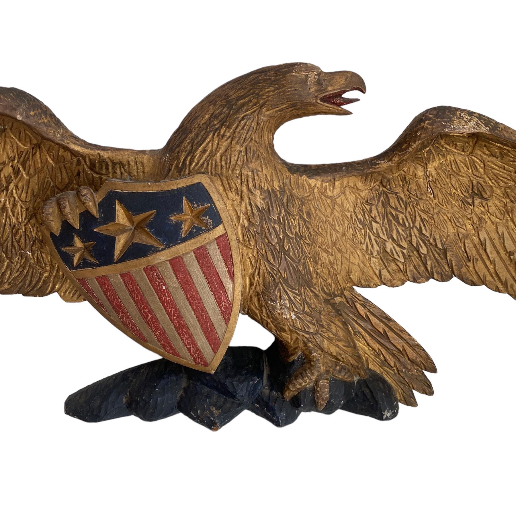 Small eagle wall plaque, spread winged, clutching an American unoin shield standing a rocky plinth. Carved from a single piece of Pine with the original polychrome and gilding with a scratched carved back. One of the wing tips was broken off at ne