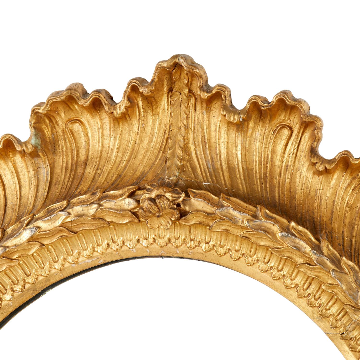 Cet exceptionnel miroir du XIXe siècle présente un cadre en bois richement doré, sculpté de manière complexe et orné de coquillages, de feuilles et de rosettes. Le miroir conserve un dos en panneau de bois et témoigne d'un travail artisanal exquis,